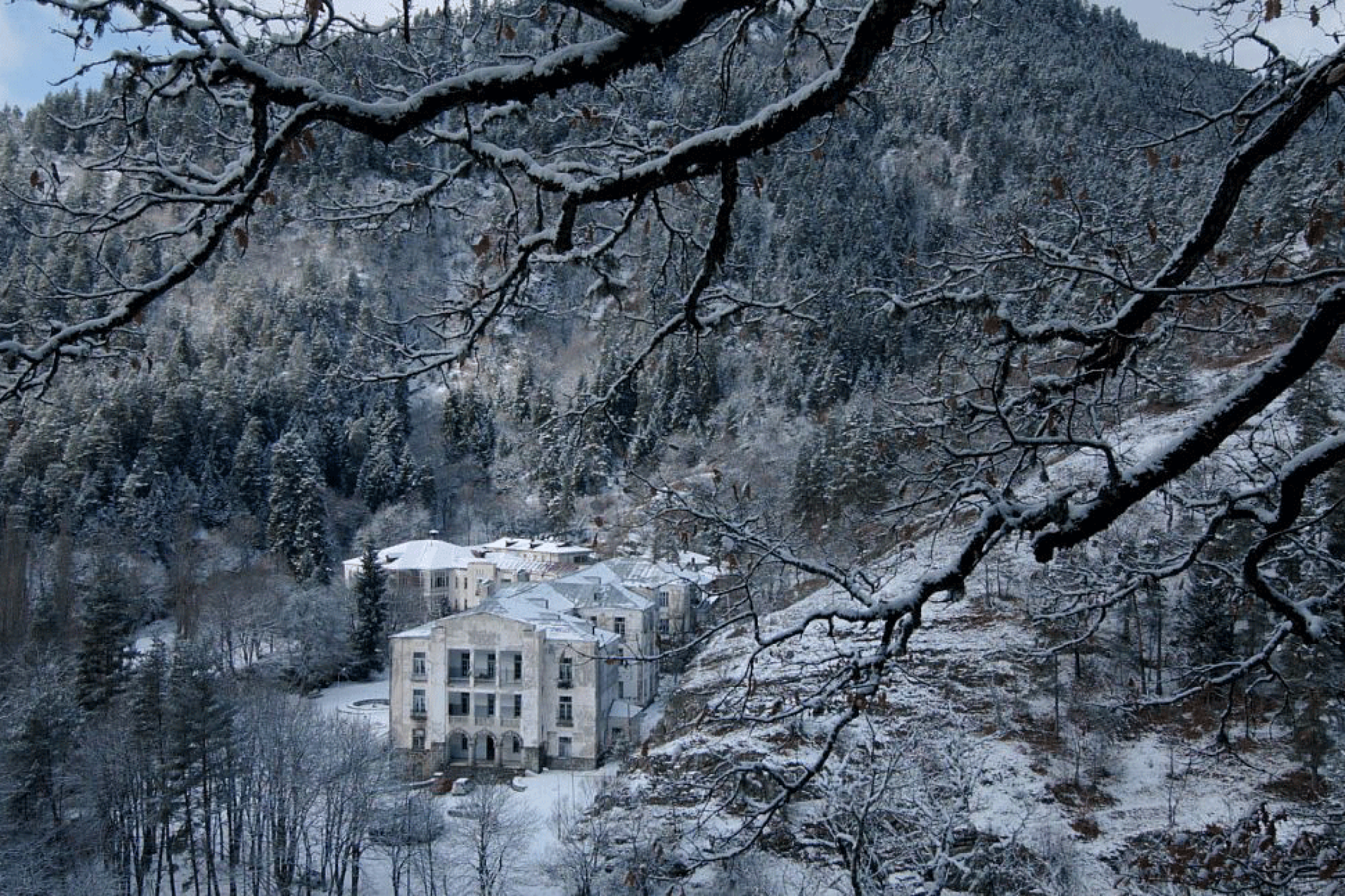 A huge building in the mountains at winter time. All is covered with snow.