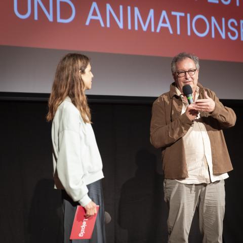 Annina Wettstein and Peter Mettler stand in front of a cinema screen and talk.