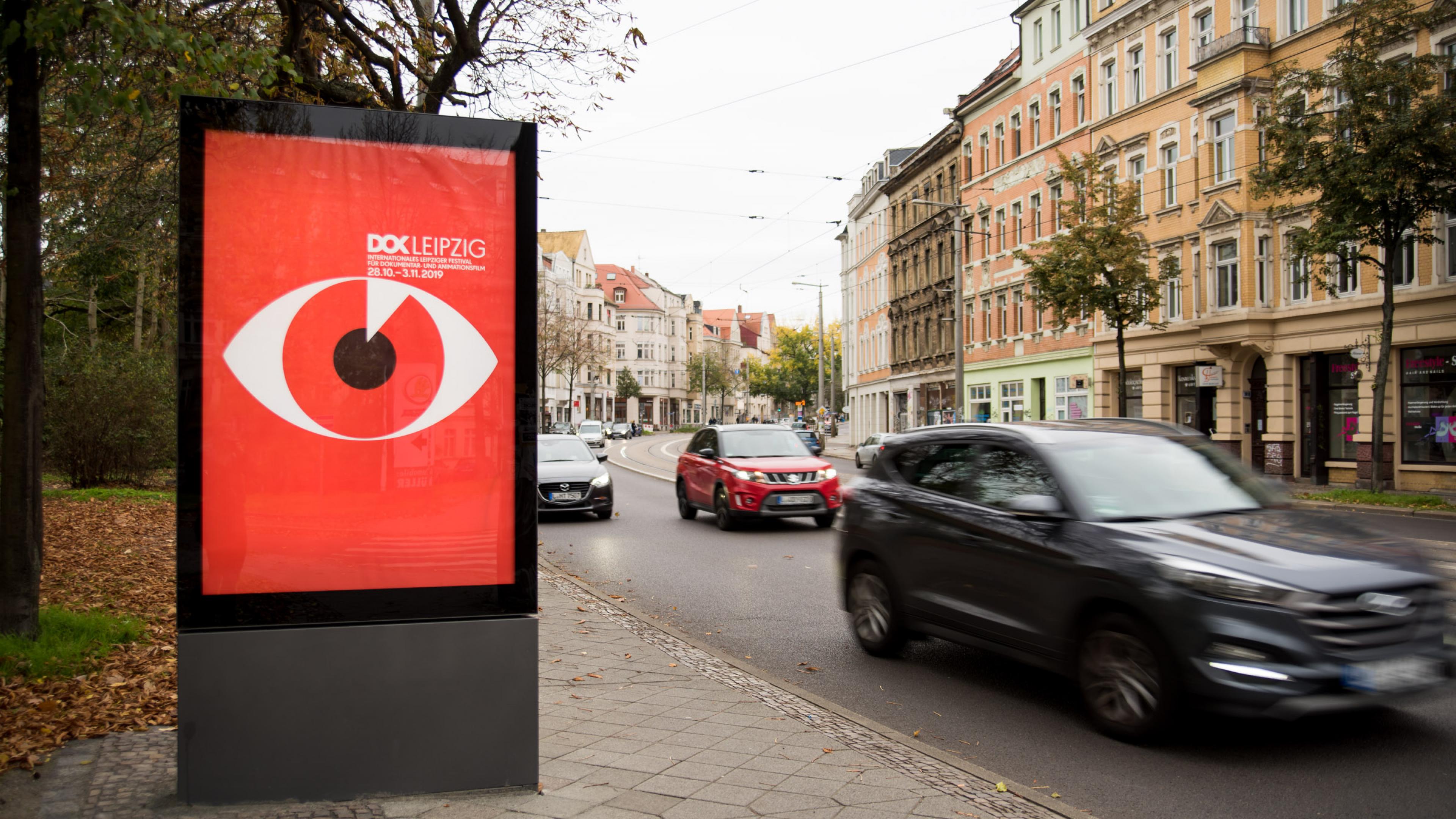 Das knallrote Festivalmotiv 2019 mit einem großen Auge mittig platziert in einem Schaukasten an der befahrenen Straße.