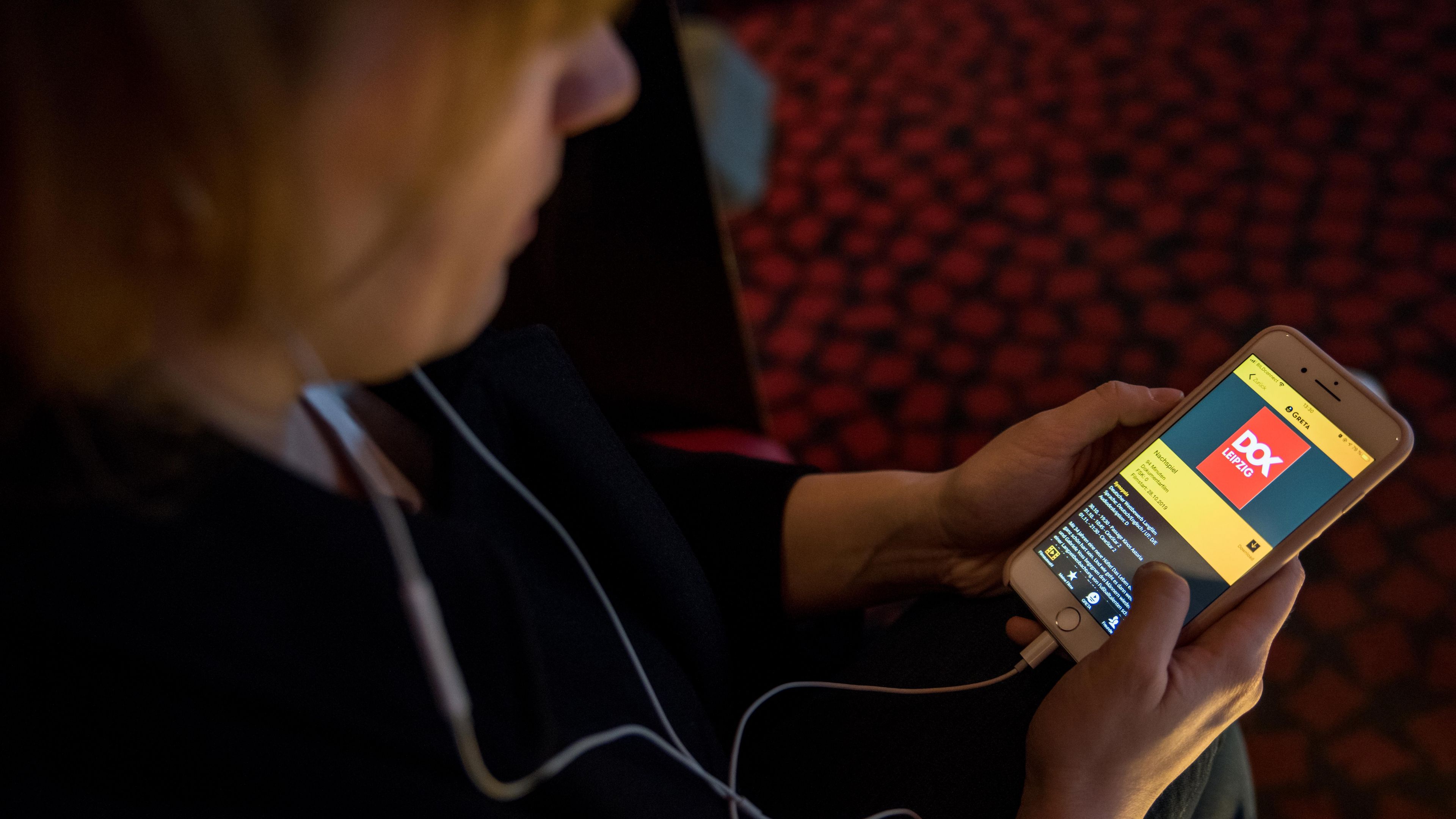 Der Betrachter sieht über die Schulter einer Frau auf einen Handybildschirm, der eine App für Audiodeskription zeigt