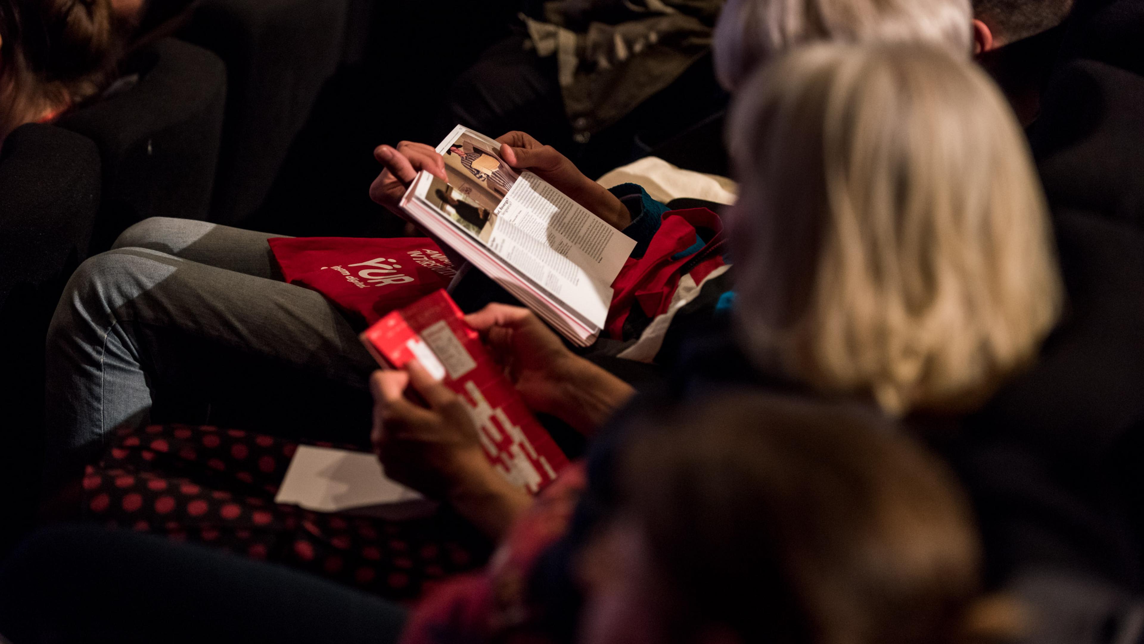 Zuschauerinnen in einer Kinoreihe lesen im DOK Leipzig Programmheft.