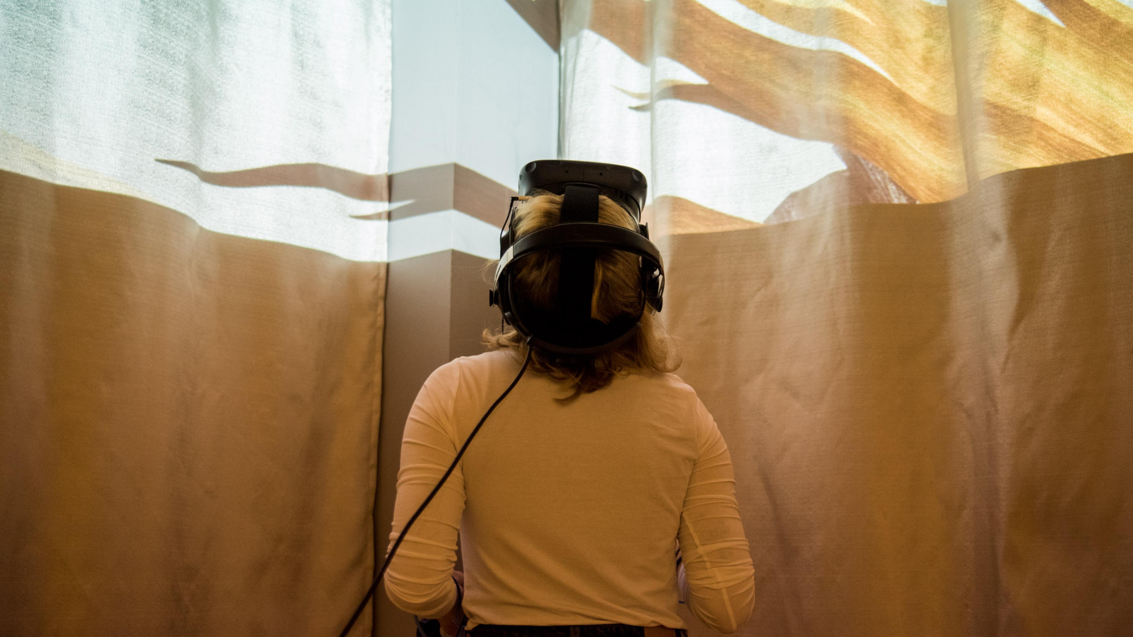 Ein weibliche Person mit VR-Brille legt ihren Kopf in den Nacken, oben im Bild erscheint eine Lichtinstallation.