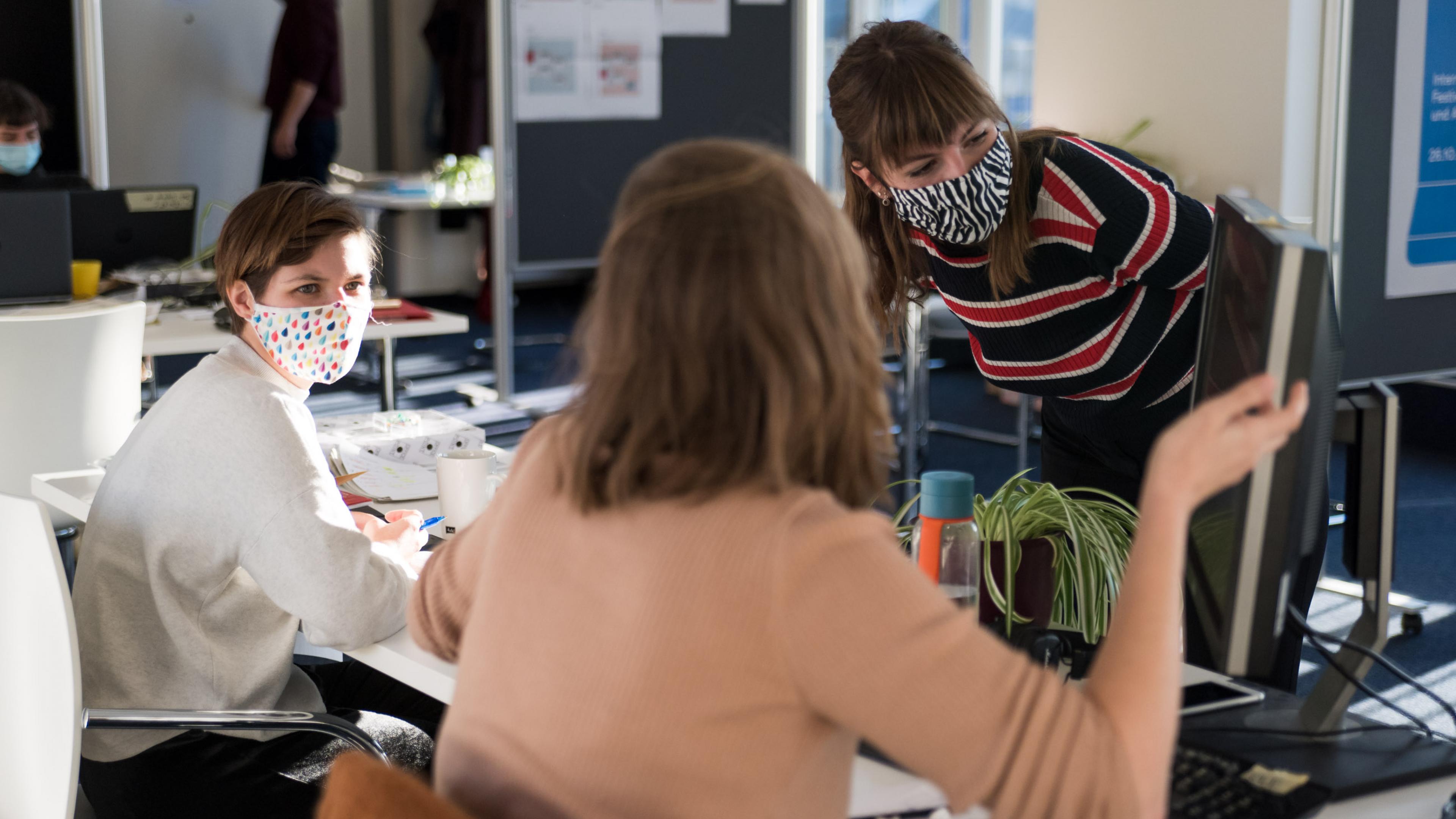Drei weibliche Personen beugen sich über einen Computerbildschirm und gestikulieren dabei.