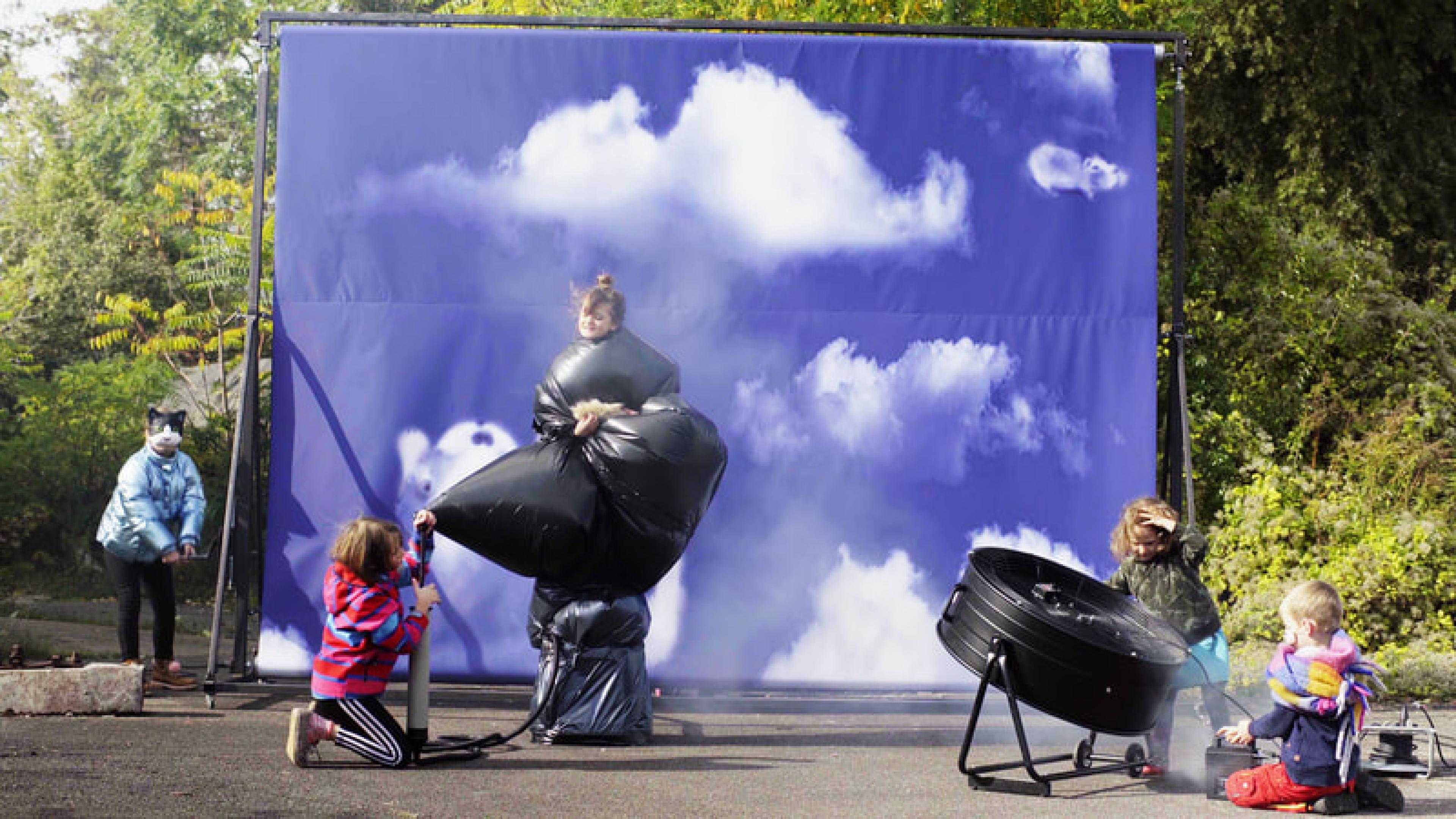 Fünf Kinder drehen in einem Filmset, im Hintergrund eine Leinwand mit Abspann, rechts steht eine Windemaschine.