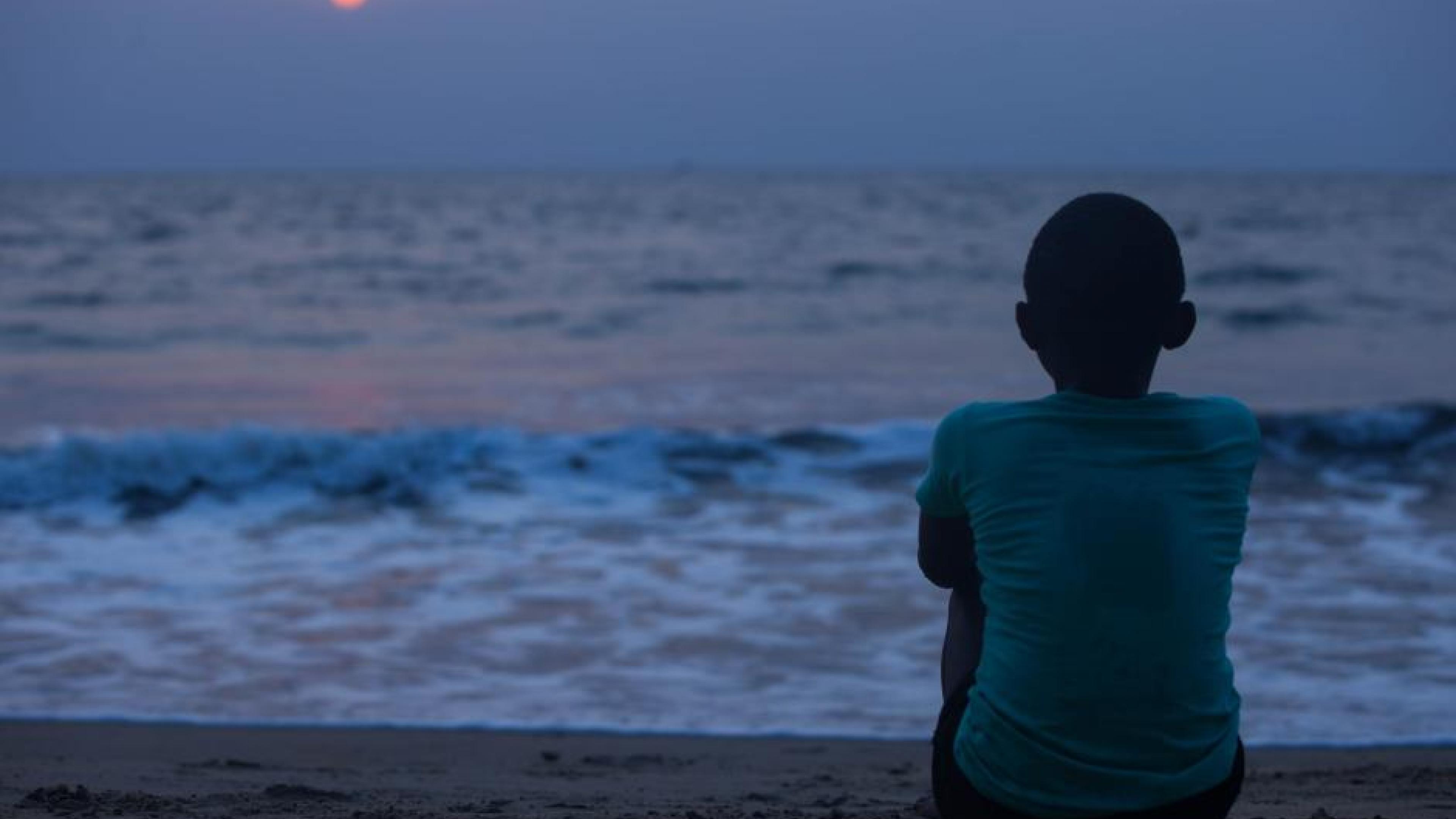Film Still from Njel. A black boy facing the sea in the sunset.