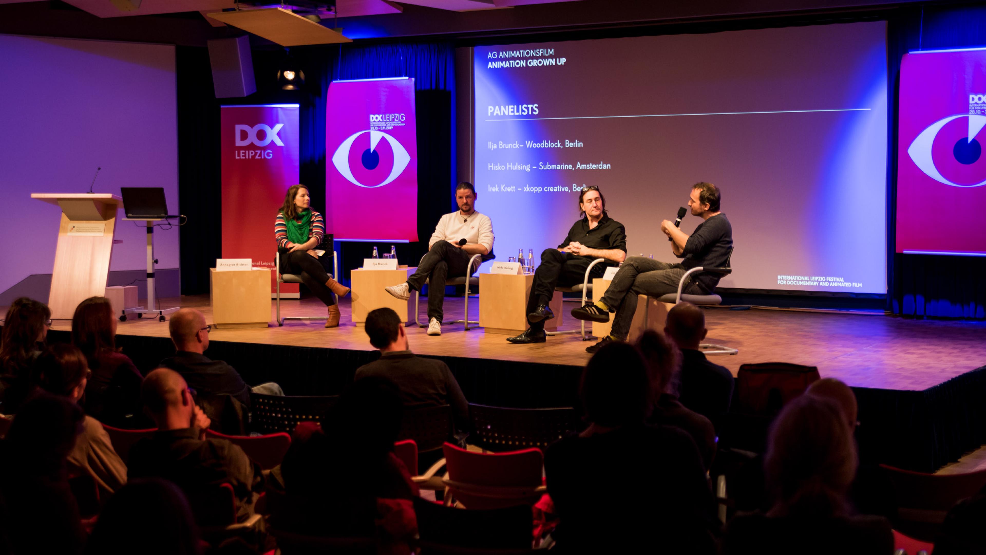 4 peple on the stage talking in front of audioence