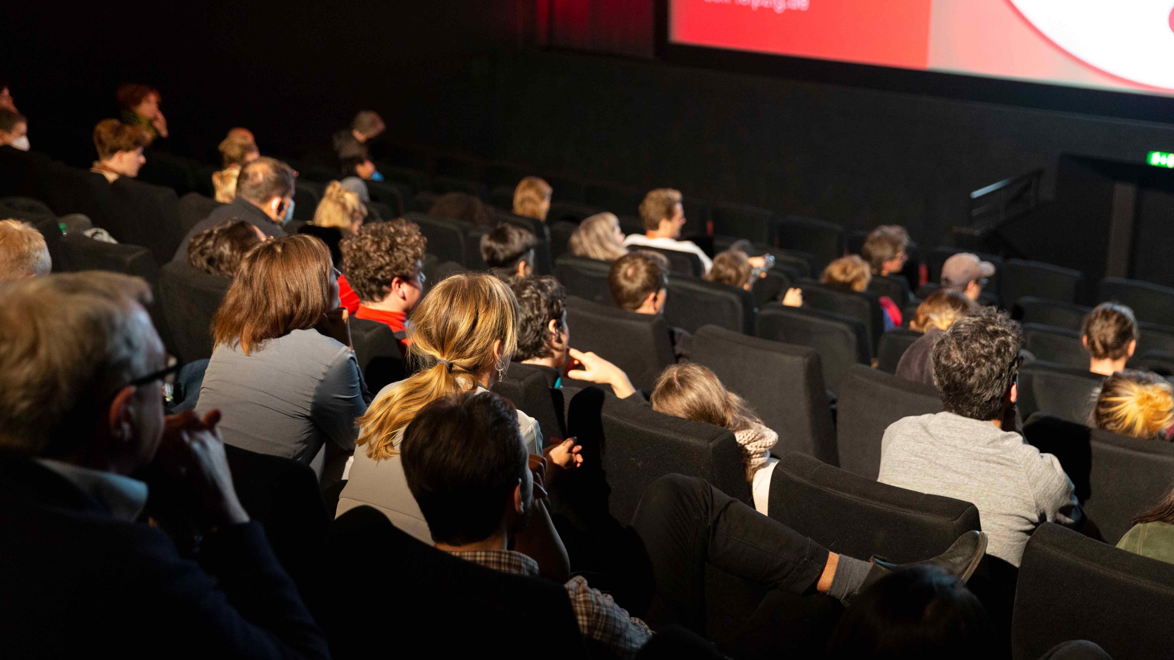 Ein Kinosaal bei einer Festivalvorführung: Blick über gut gefüllte Zuschauerreihen Richtung Leinwand. Viele Zuschauer*innen lehnen sich interessiert nach vorne.