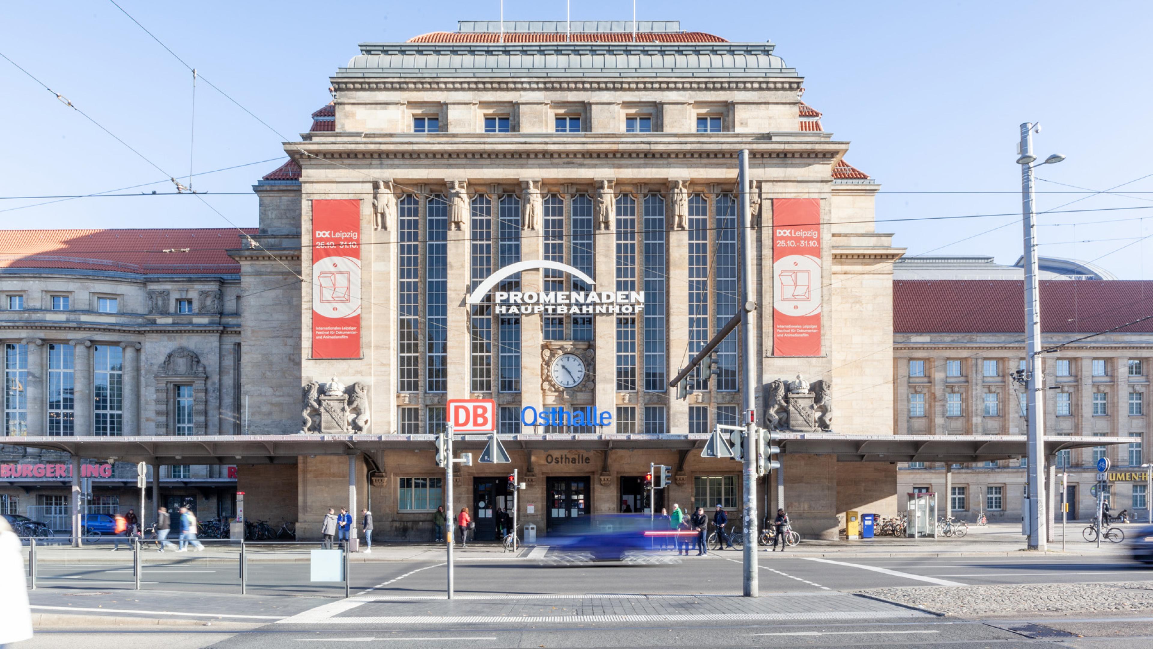 Blick auf den Vorplatz und die Osthalle des Leipziger Hauptbahnhofs. Links und rechts neben dem Eingang zwei rote Banner von DOK Leipzig.