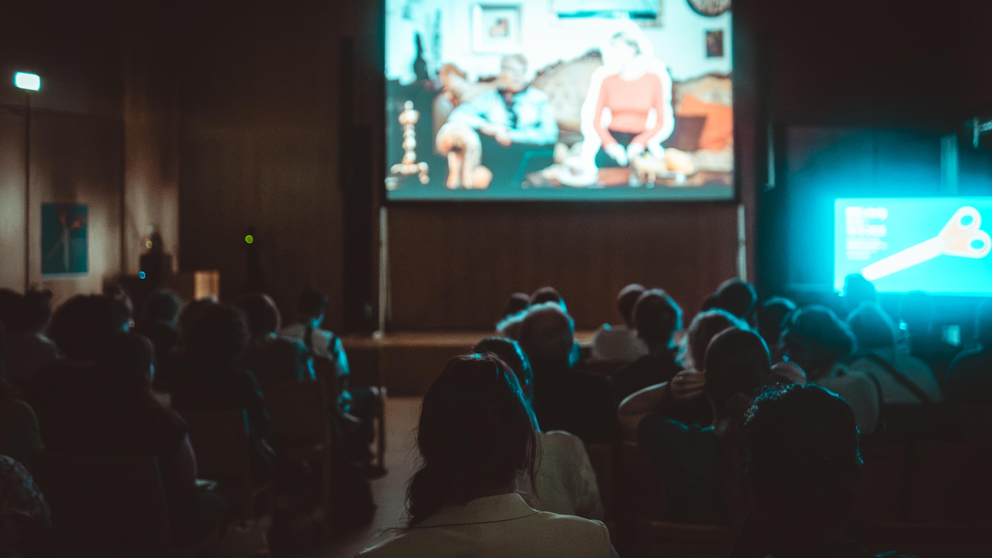 Audience in a screening room is watching a film on a big screen.