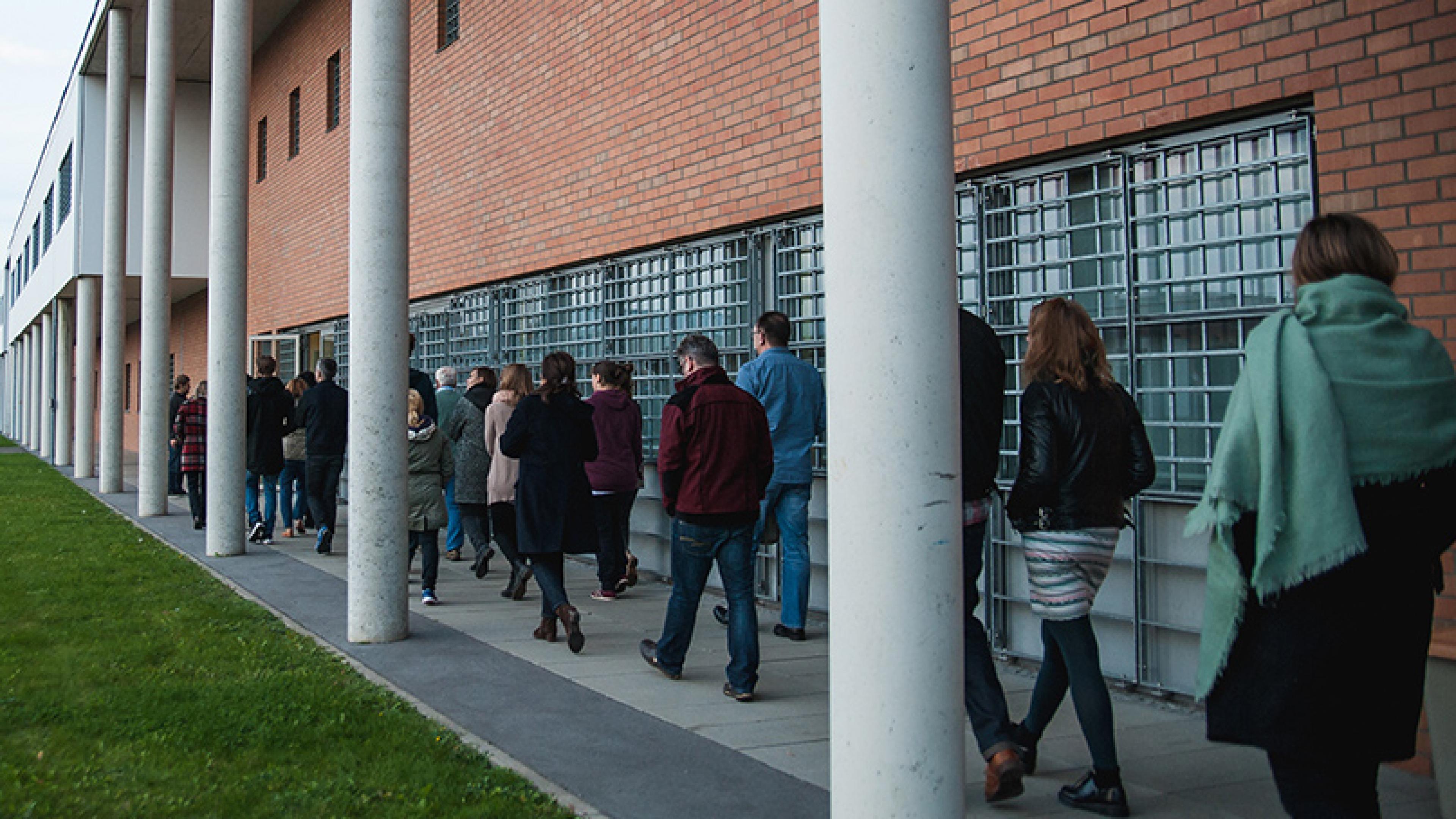 Mehrere Personen gehen an einem Gebäude mit vergitterten Fenstern entlang.