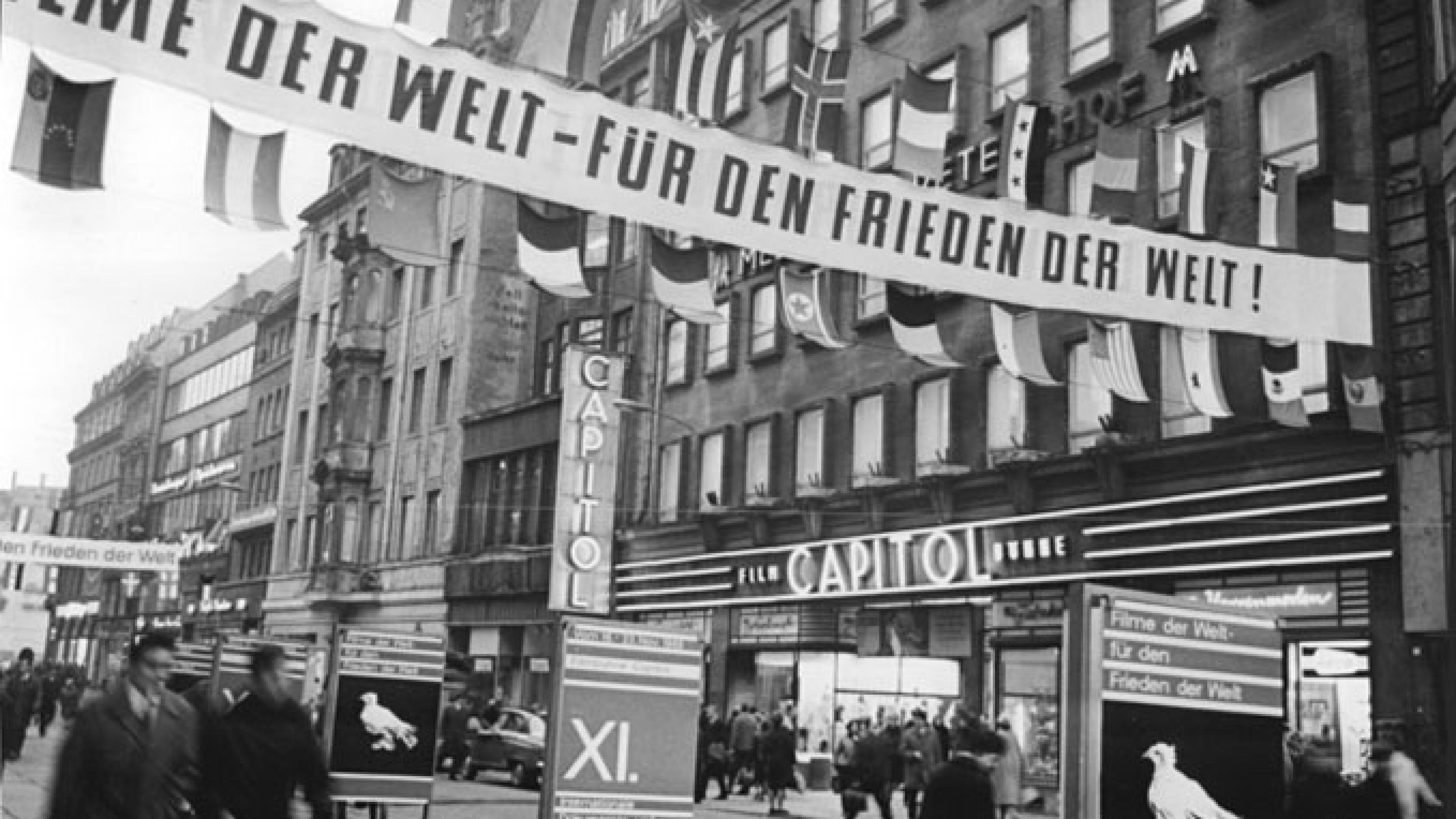 Die Petersstraße in Leipzig. Über der Straße hängt ein Banner mit dem Text "Filme der Welt für den Frieden der Welt".