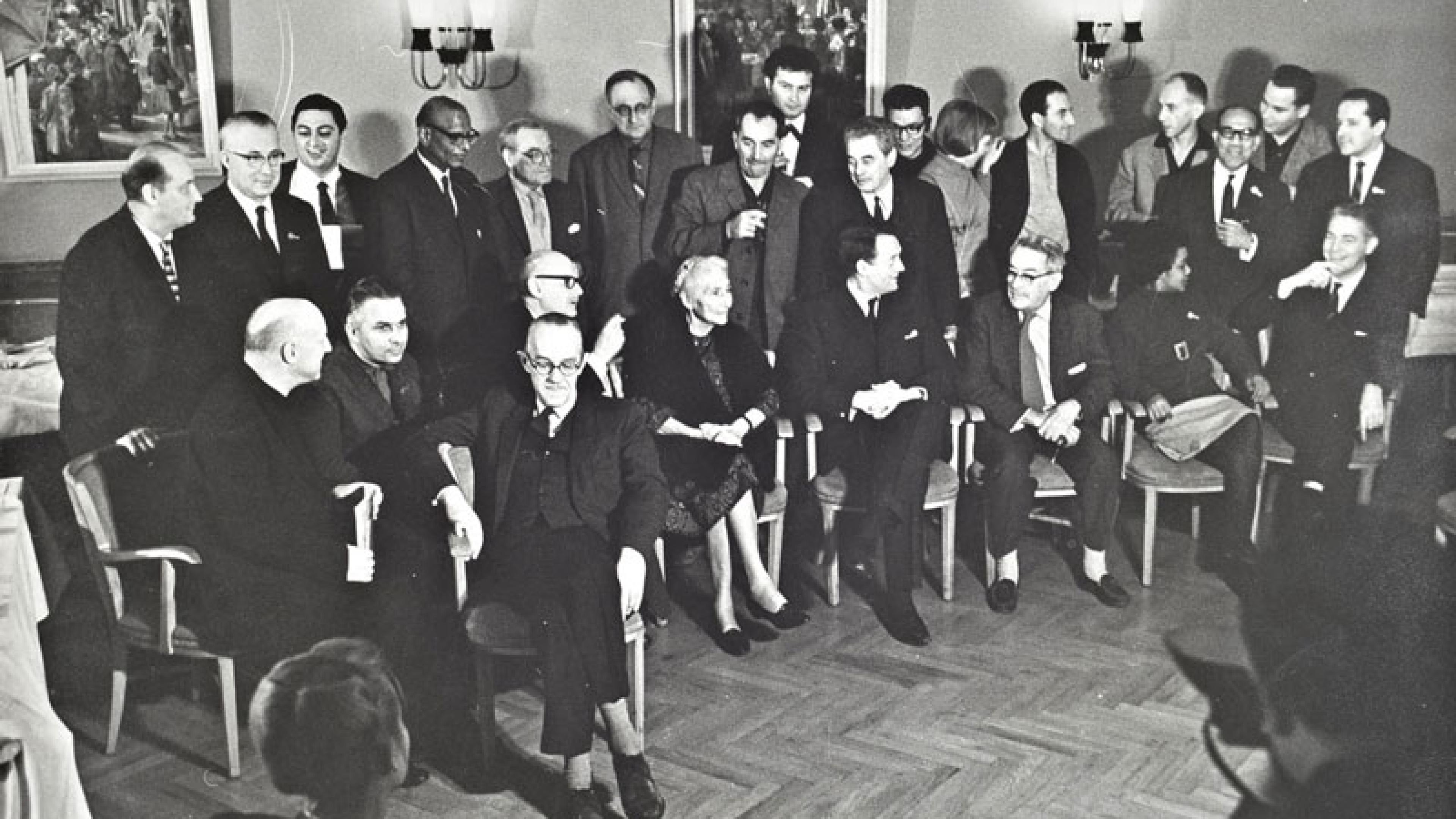 Rund zwei Dutzend Personen in zwei Reihen (vorne sitzend, dahinter stehend) bei einer Pressekonferenz.