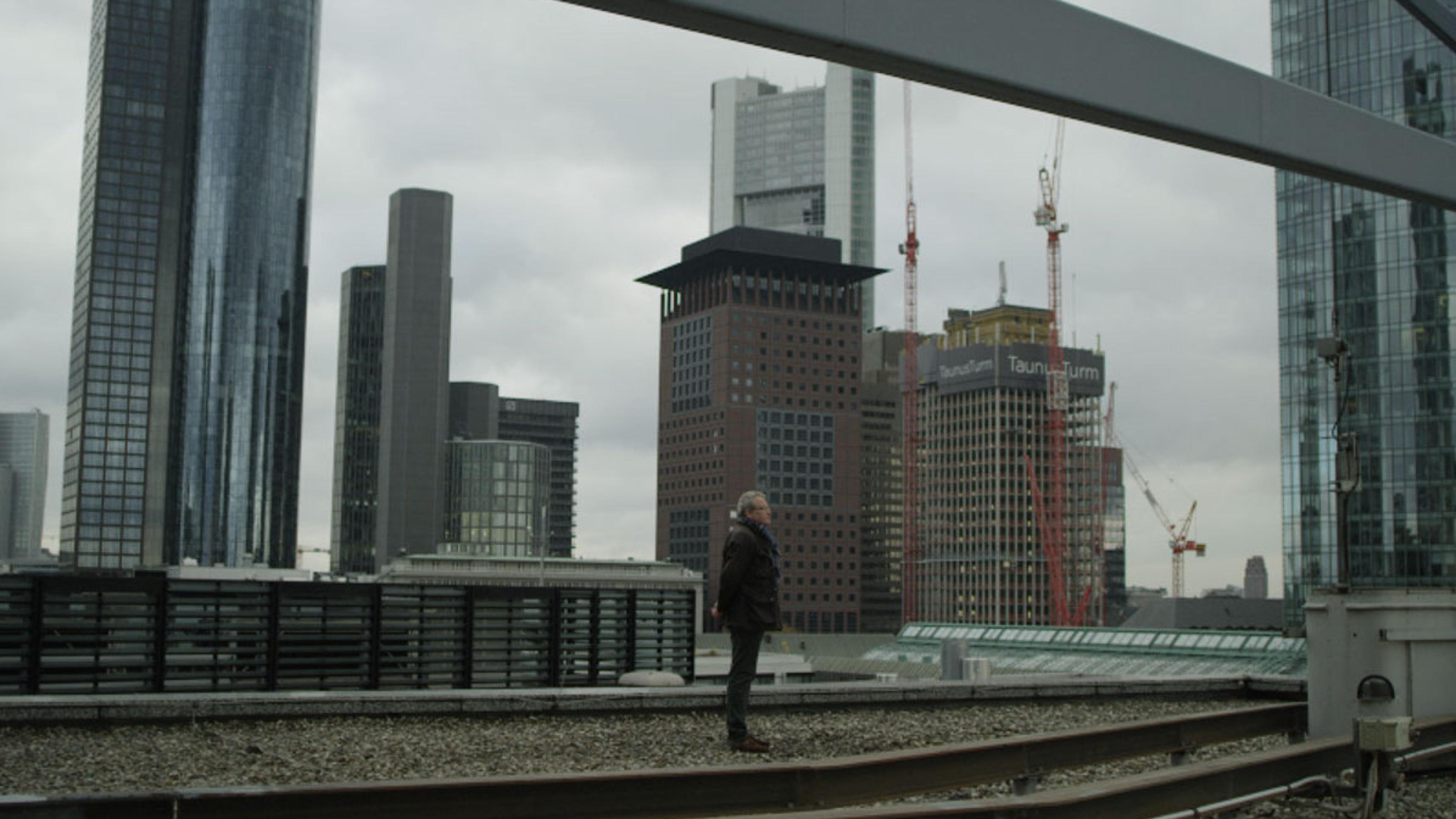 Ein Mann steht auf einem Gebäudedach inmitten der Skyline von Frankfurt.