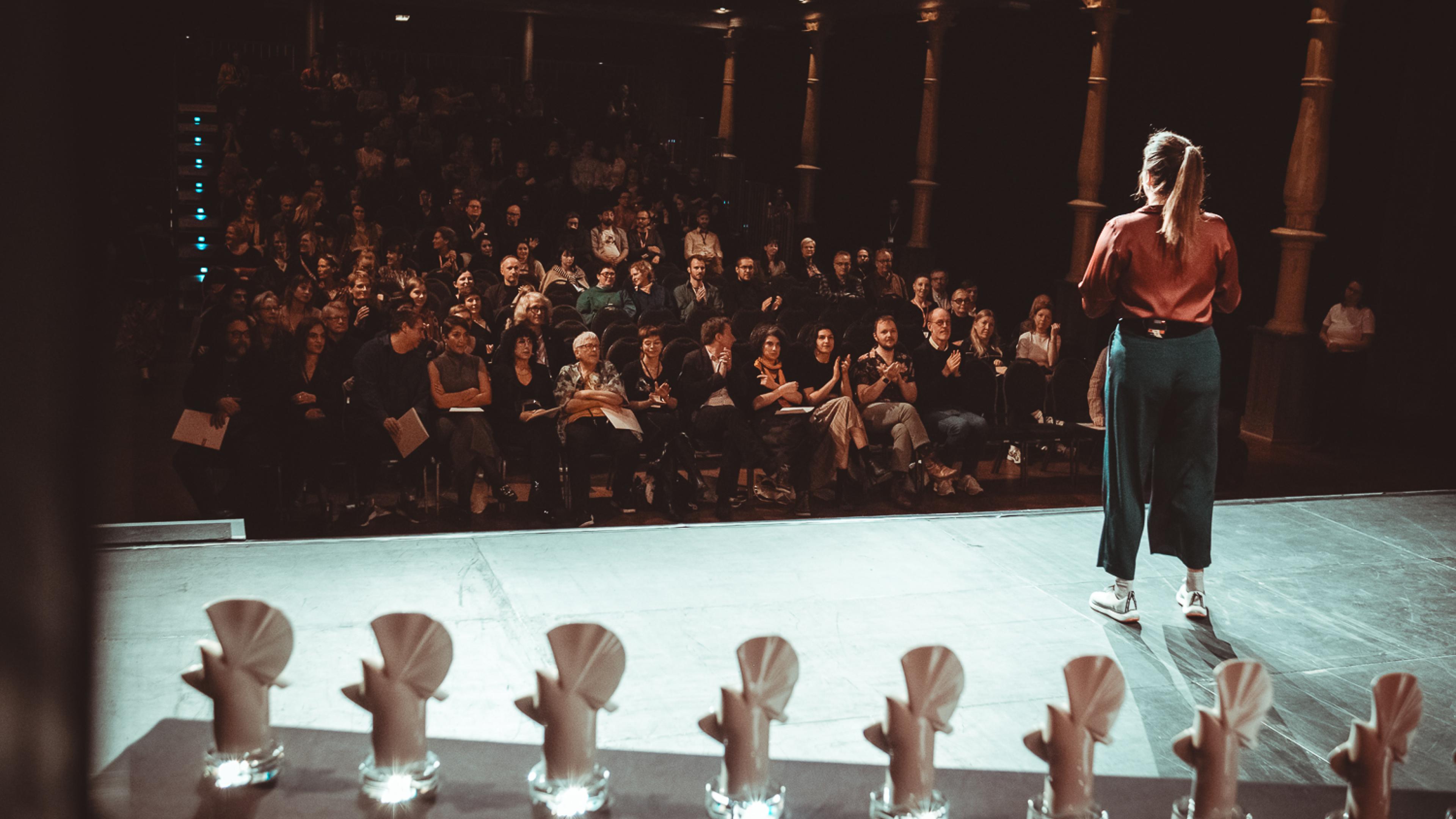 Der Schaubühne Saal voller Publikum, auf der Bühne steht eine Moderatorin und fein säuberlich sieben Goldene und Silberne Tauben