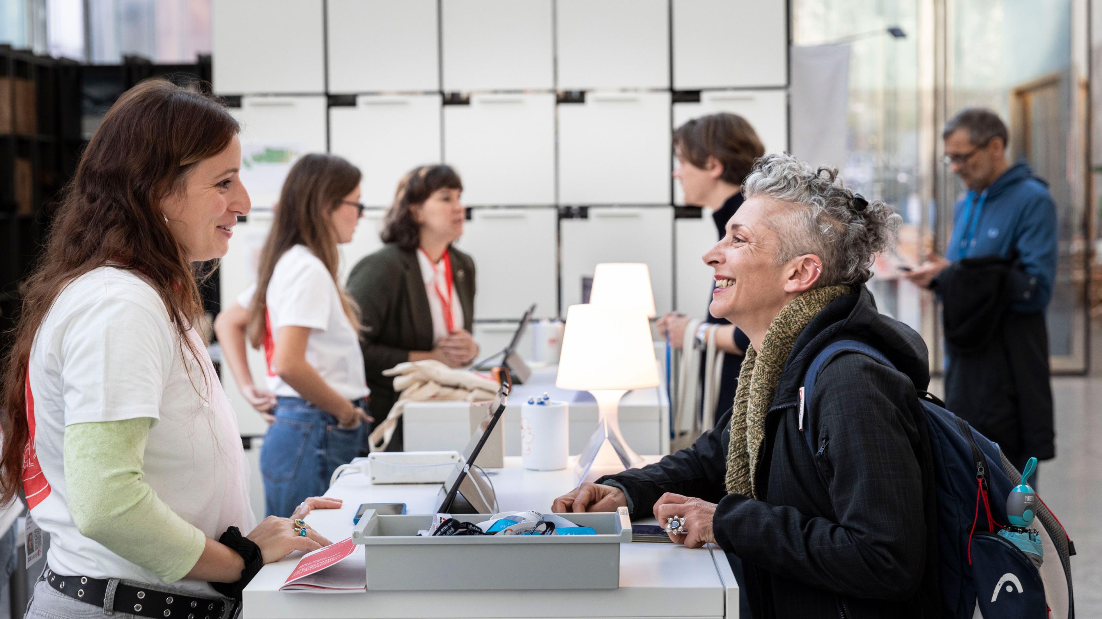 At the Dok Counter, a team member and an accredited guest are smiling broadly at each other