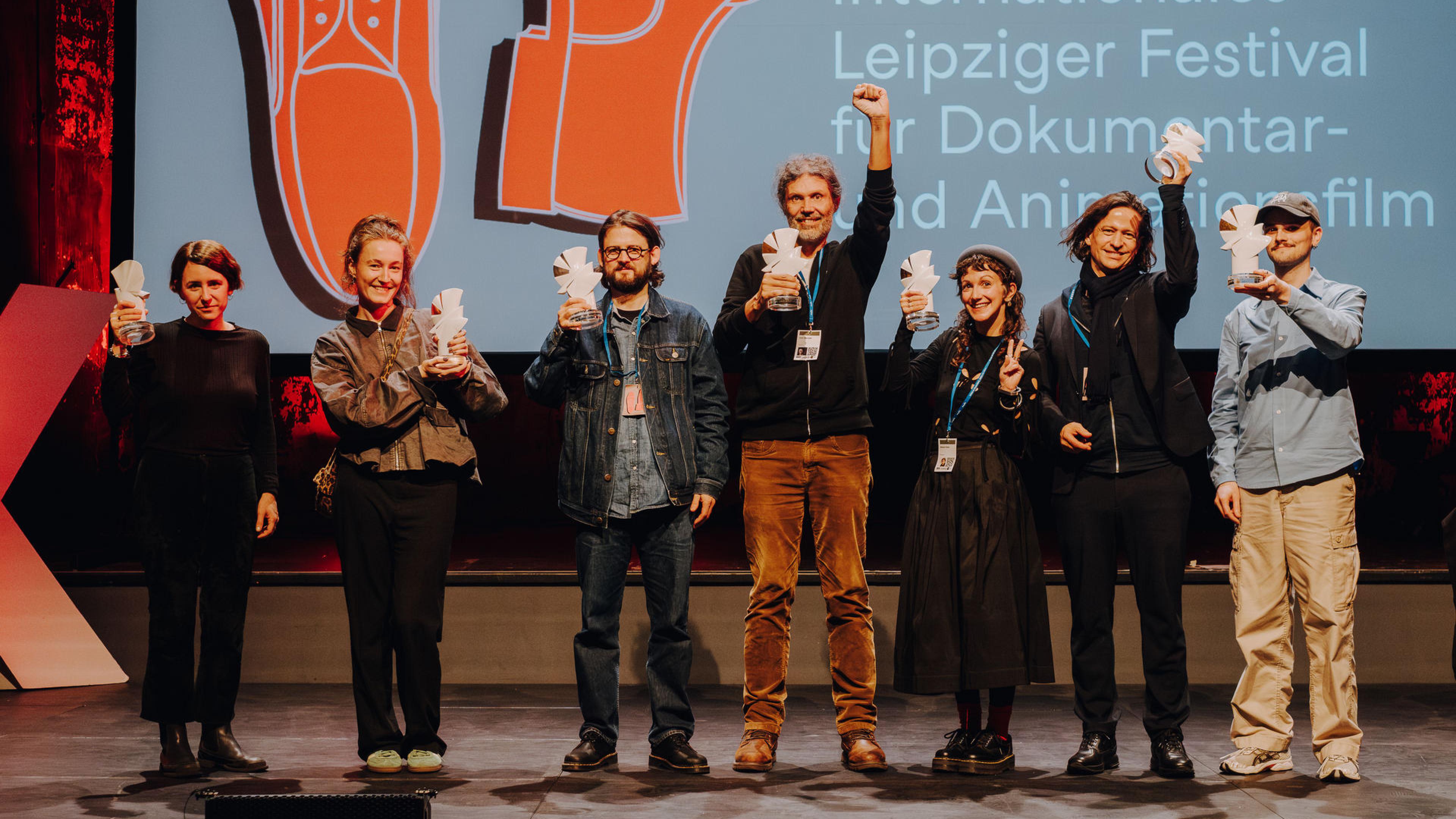 Gruppe von Personen auf Bühne, die ihre Tauben-Preise in die Luft halten