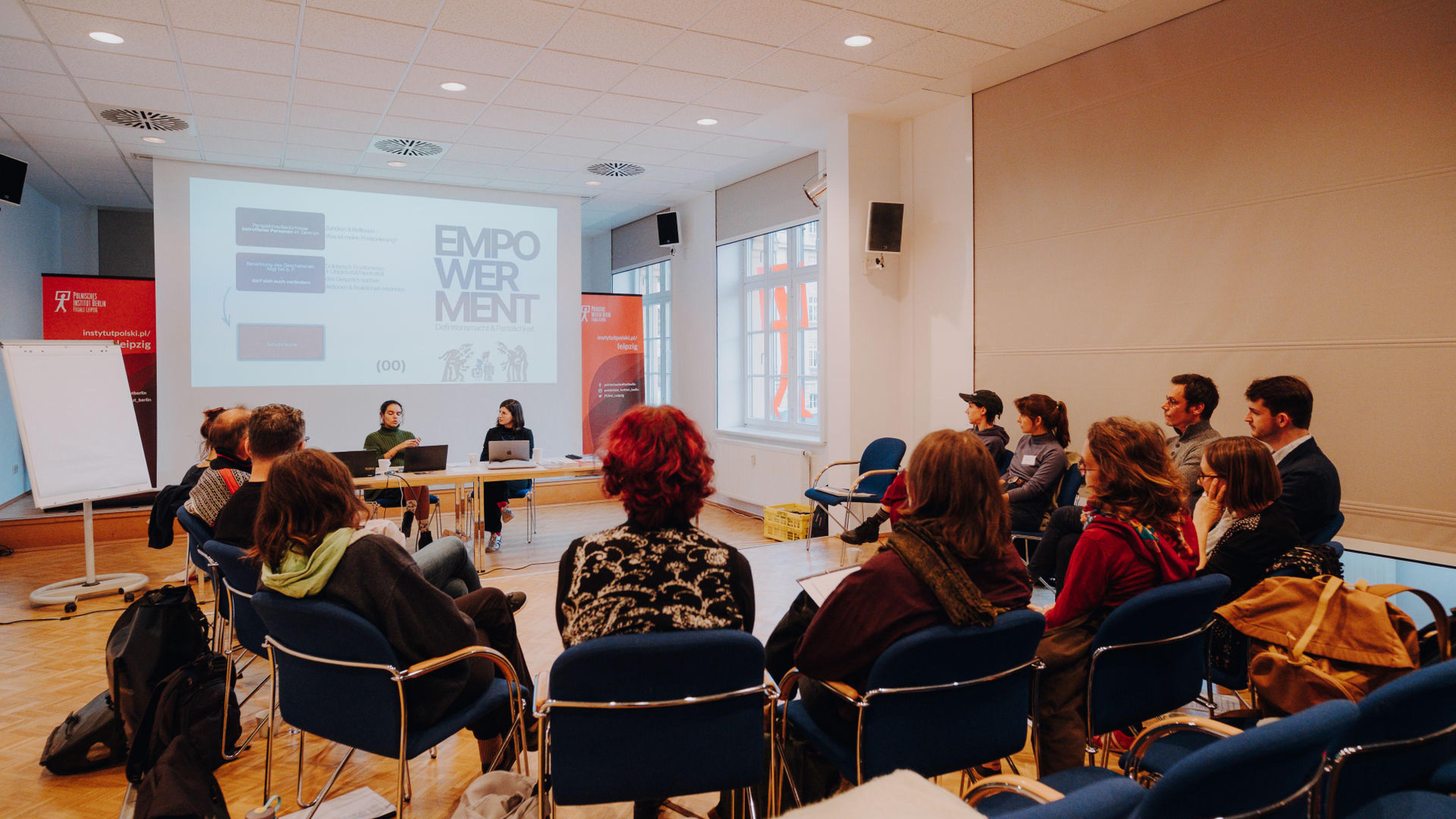 Ein Dutzend Menschen sitzen im Kreis in einem Seminarraum, vorne steht auf einer Leinwand das Wort Empowerment