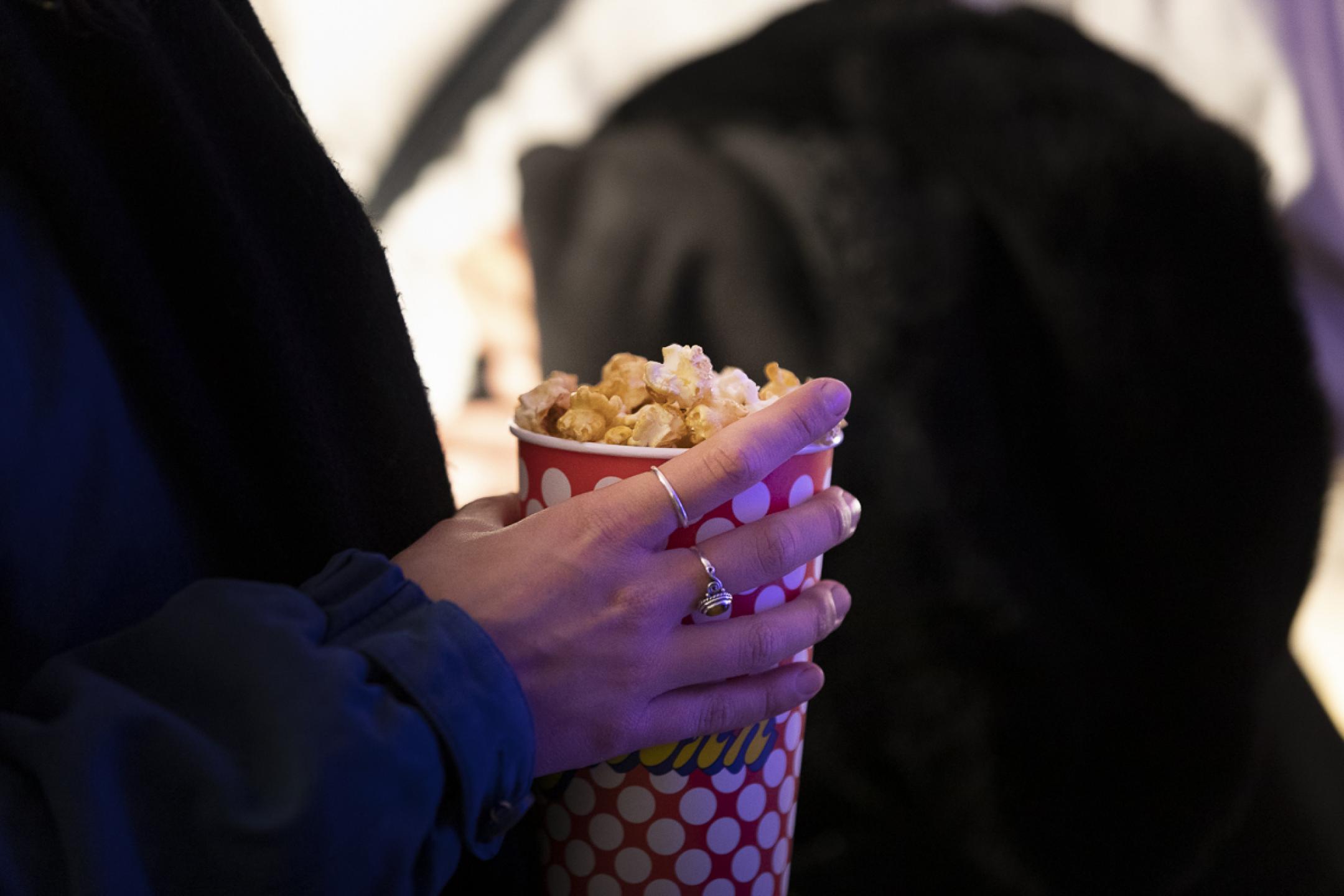 Nahaufnahme einer Hand, die einen Becher voller Popcorn trägt.