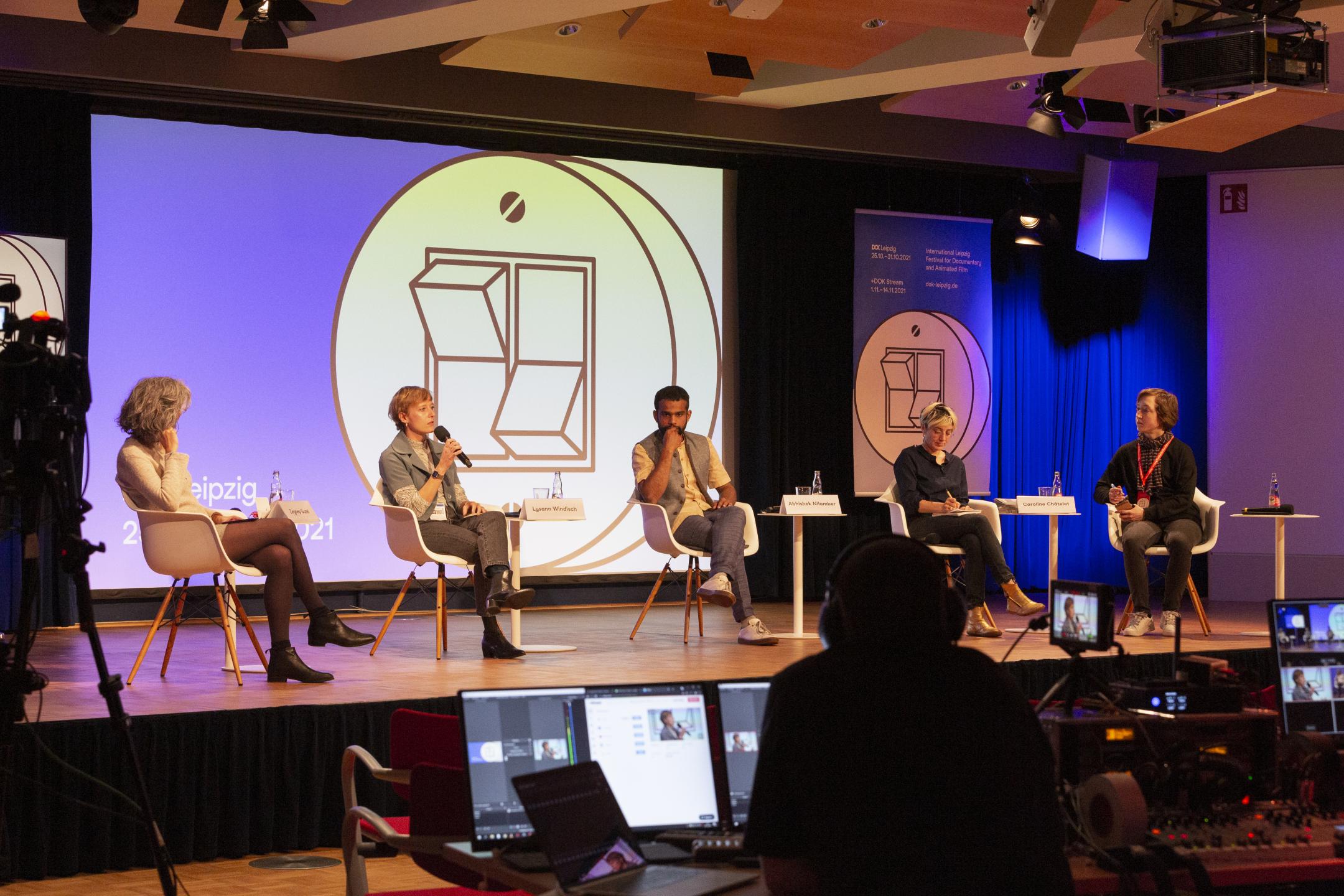 5 people sitting on chairs on the stage, background Dok Industry switch motif