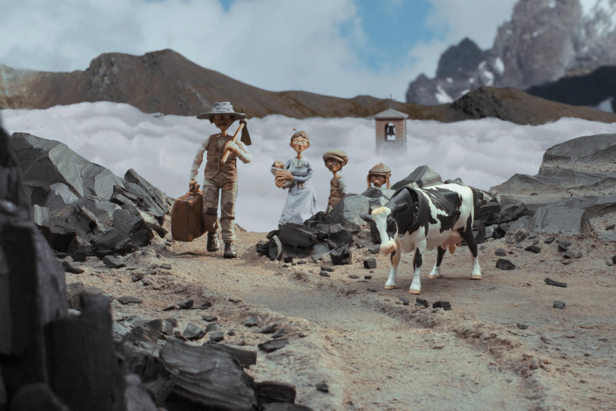 Ein Animationsfilmstill. Vier Puppenfiguren und eine Kuh stehen in einer steinigen Berglandschaft, hinter ihnen ist eine Schlucht voller Wolken, nur ein Kirchturm schaut heraus. Die Vaterfigur läuft mit Spitzhacke und Koffer in den Händen auf die Kamera zu, die Mutter mit Baby im Arm und zwei Jungen schauen ihm hinterher