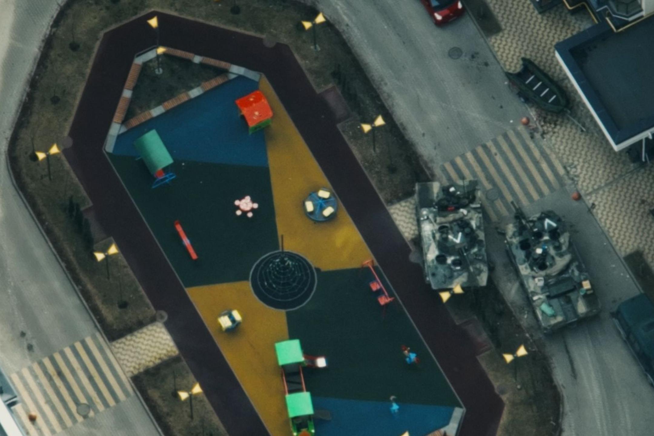 A bird’s eye view on a place in a city environment. Two tanks are crossing the place, a few cars are parking at the side. No people.