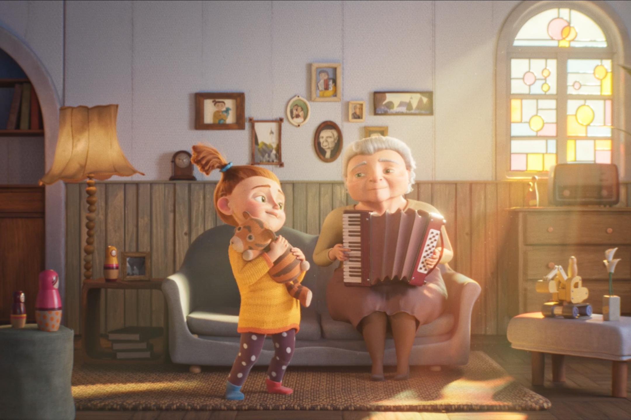 Filmstill aus einem Animationsfilm: Eine ältere Frau mit grauen Haaren sitzt auf einem Sofa in einem Wohnzimmer und spielt Akkordeon. Vor dem Sofa steht ein Mädchen mit roten Haaren und einem Zopf. Es hält ein Kuscheltier im Arm. Die Frau und das Mädchen haben beide ihren Kopf leicht zur Seite geneigt und lächeln sich an.