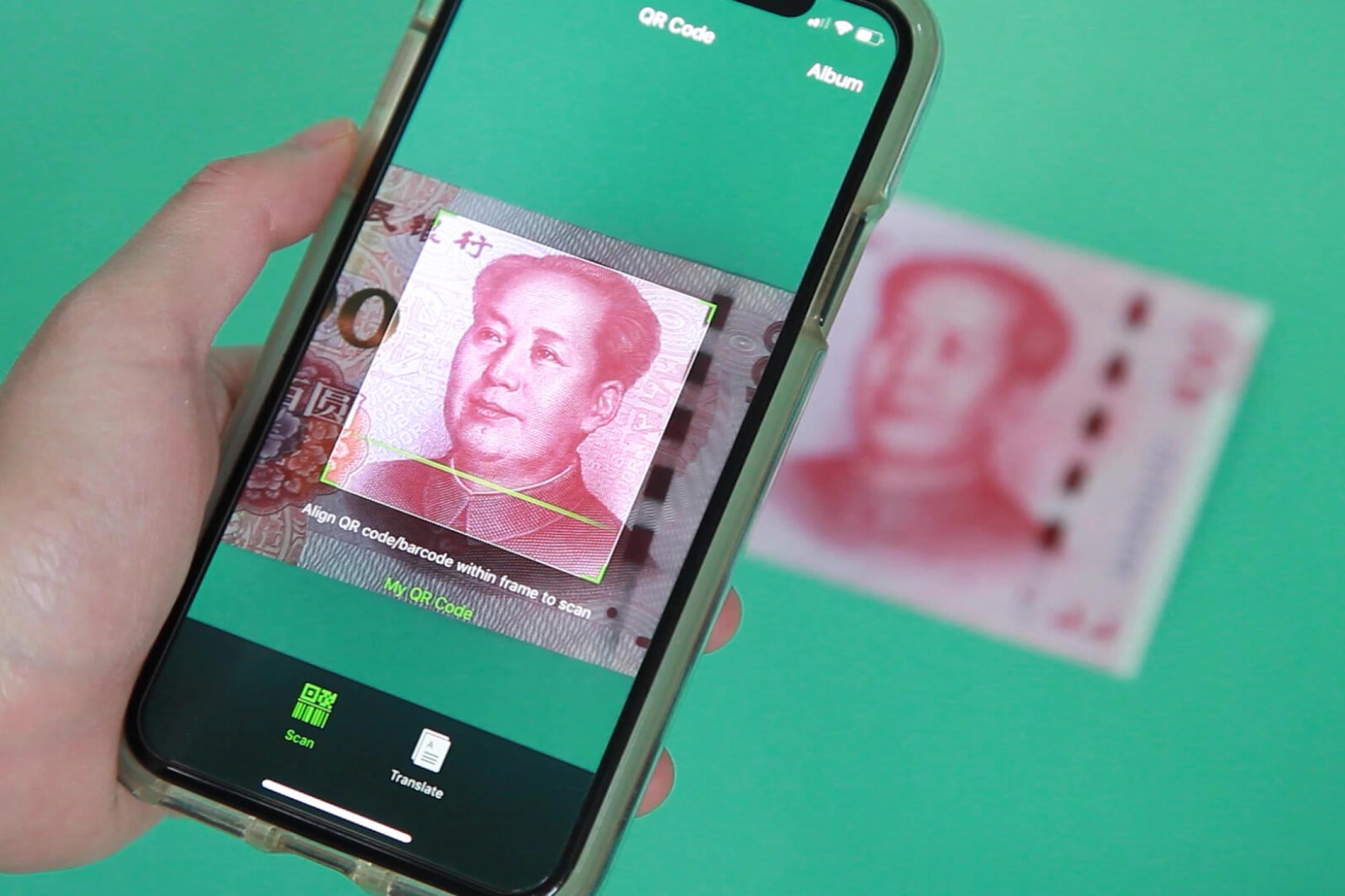 Eine Hand scannt mit einem Smartphone das Portrait von Mao auf einen chinesischen Geldschein