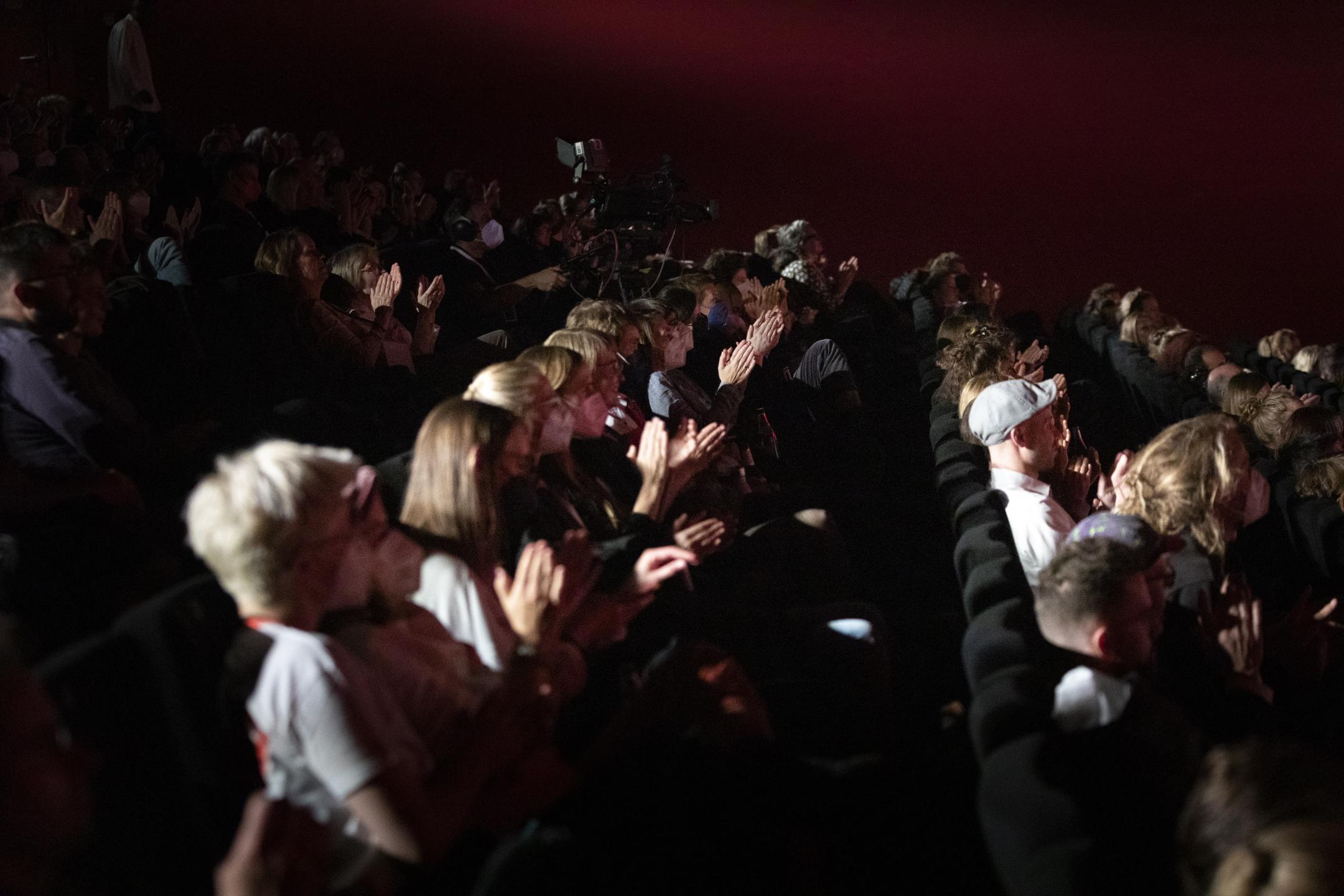 Vollbesetzte Zuschauerreihen in einem Kino. Das Publikum applaudiert, viele lächeln.