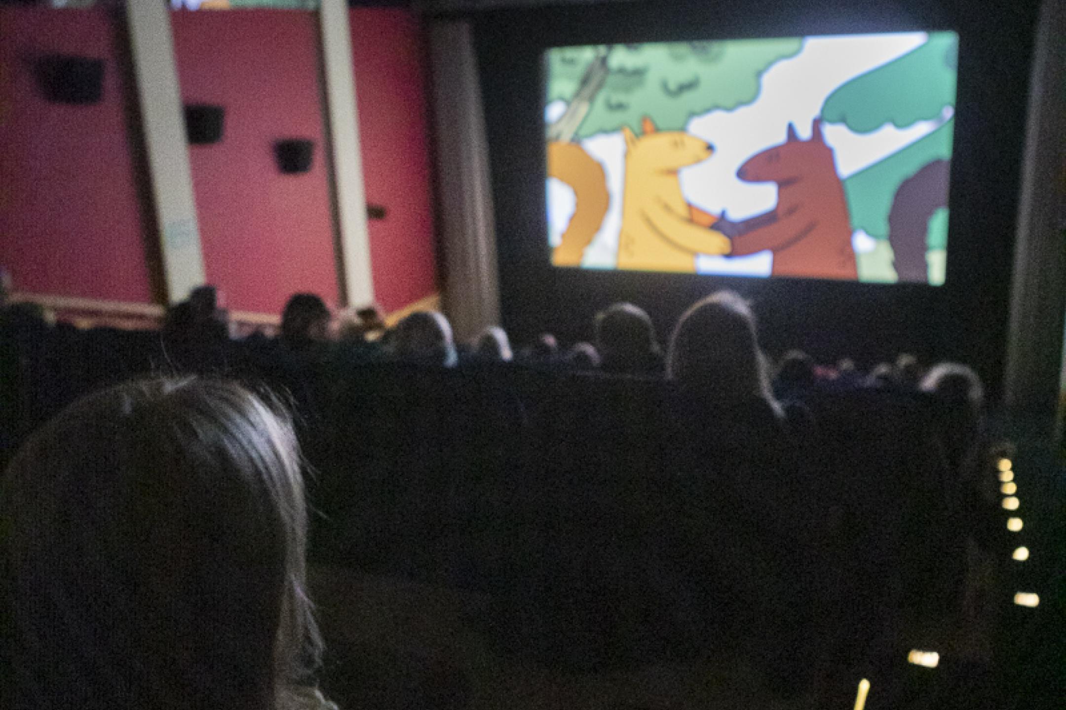 Eine Kinovorstellung für Kinder: Auf der Leinwand zwei fassen sich zwei Eichhörnchen als Zeichentrickfiguren an den Händen. 
