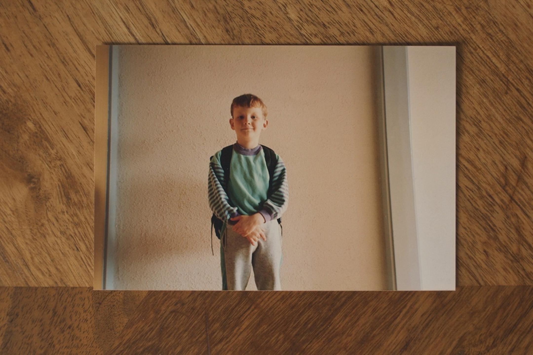 A portrait photo of a young boy lies on a wooden table.