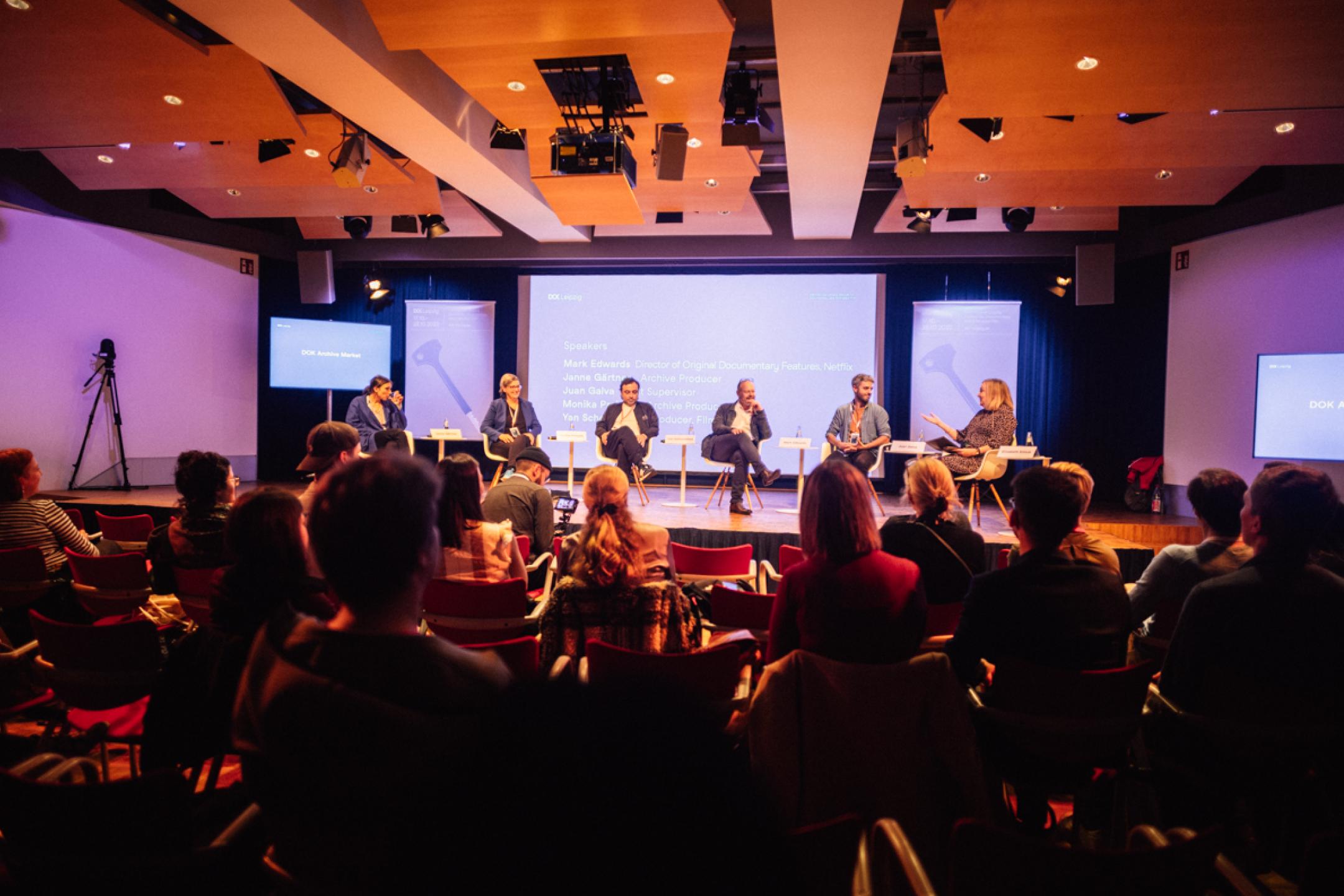 A panel with six persons sit in front of a panel.