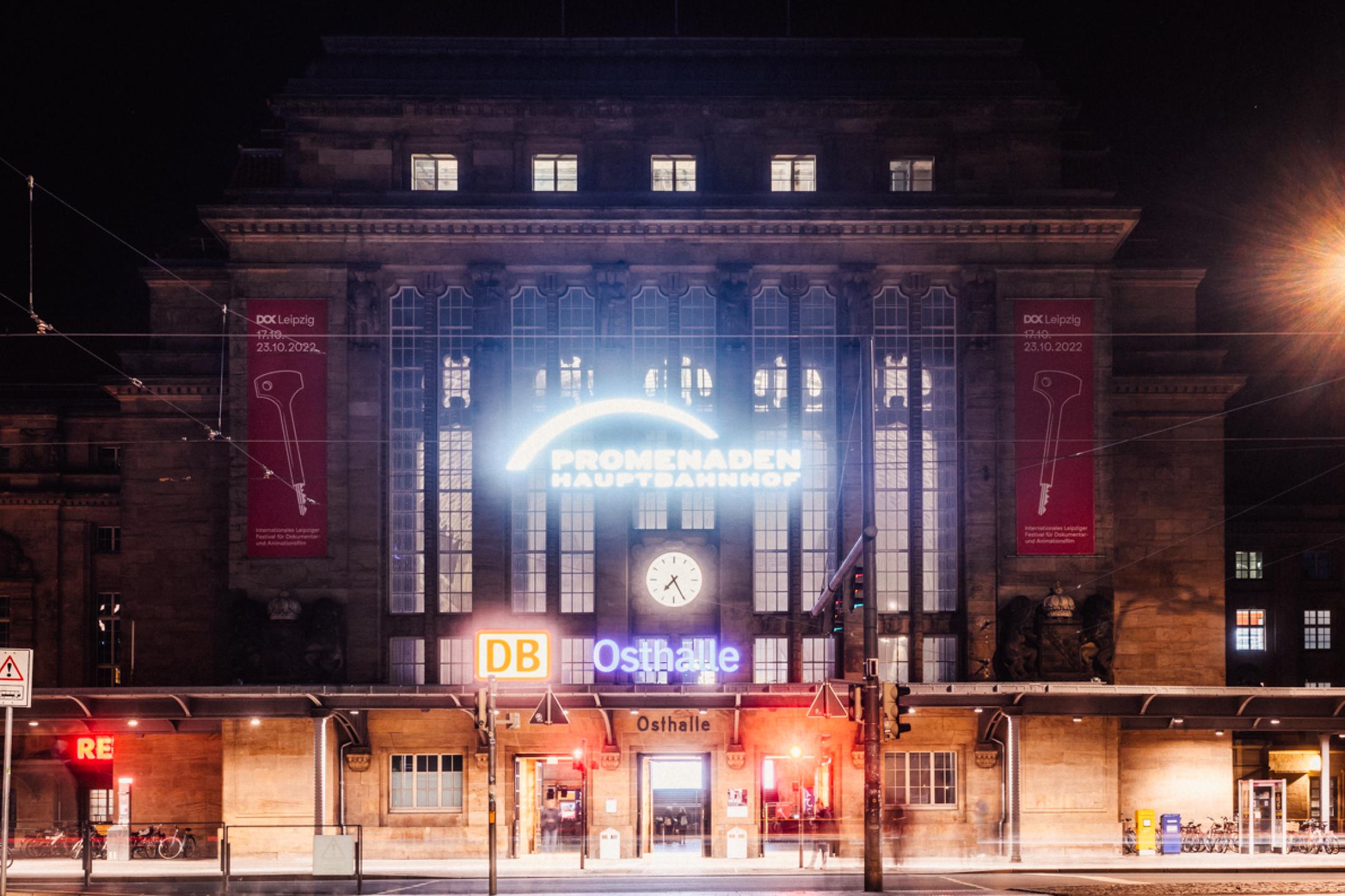 Das Hauptbahnhof-Gebäude in Leipzig von außen bei Nacht. Über dem Eingang leuchtet das Schild "Osthalle".