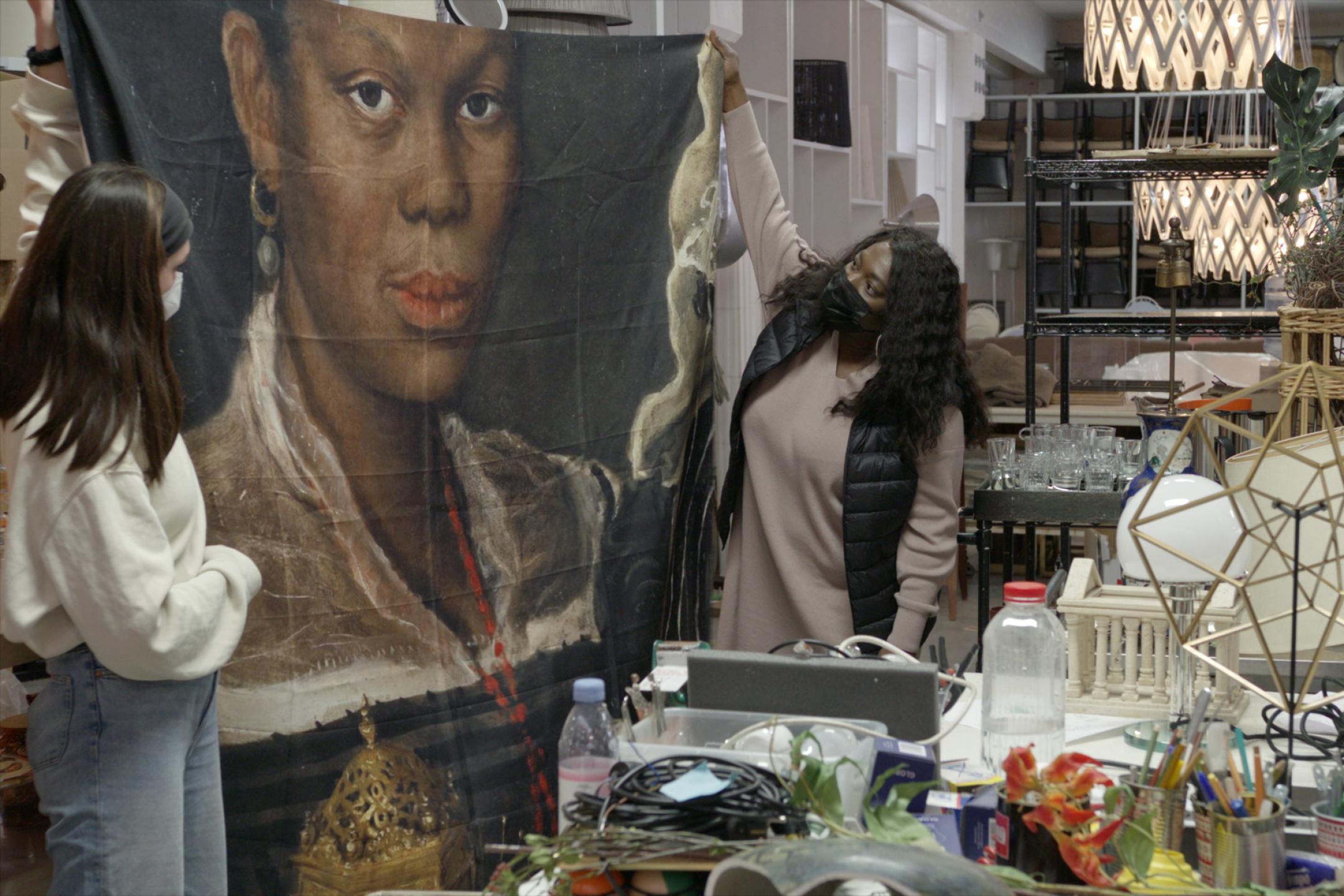 Zwei Frauen halten ein großes Tuch mit dem Porträt einer Schwarzen Frau hoch.