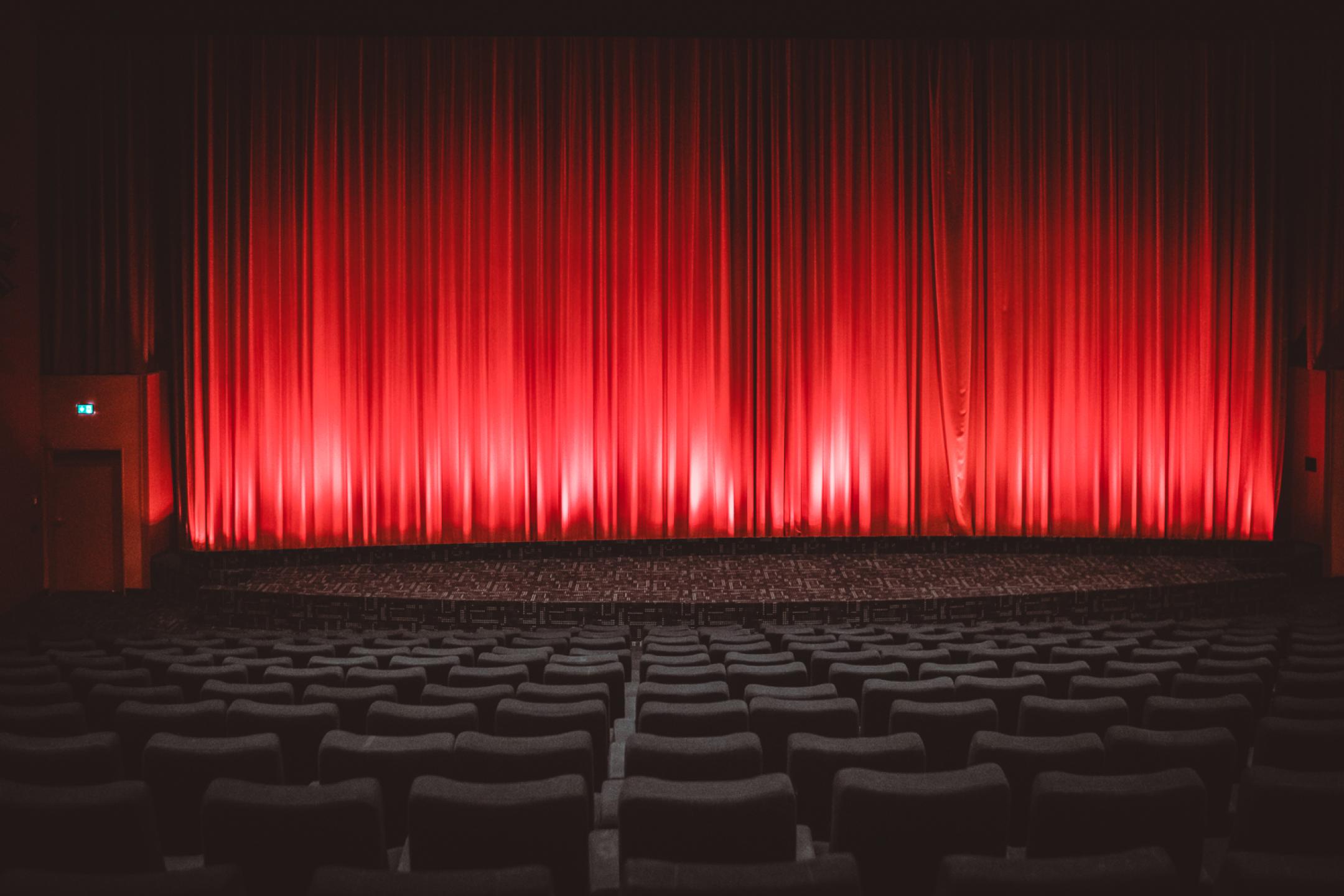 Ein komplett leerer Kinosaal. Vor der Leinwand ein roter Vorhang, der angeleuchtet wird.