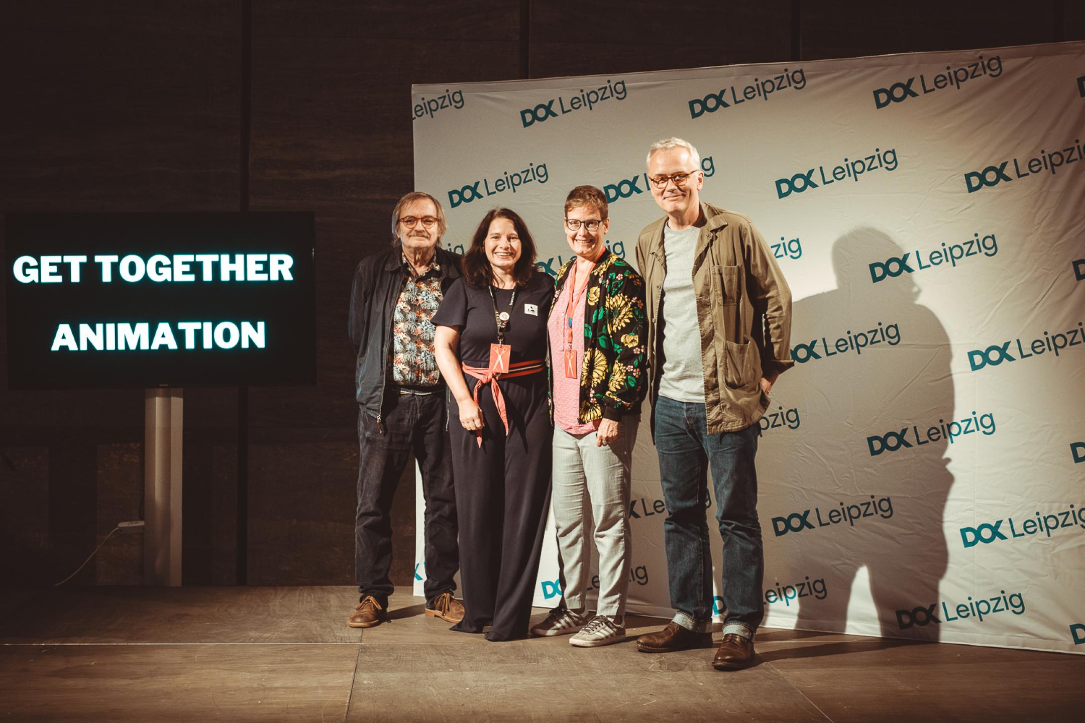 Four persons pose together in front of a DOK Leipzig logo banner.