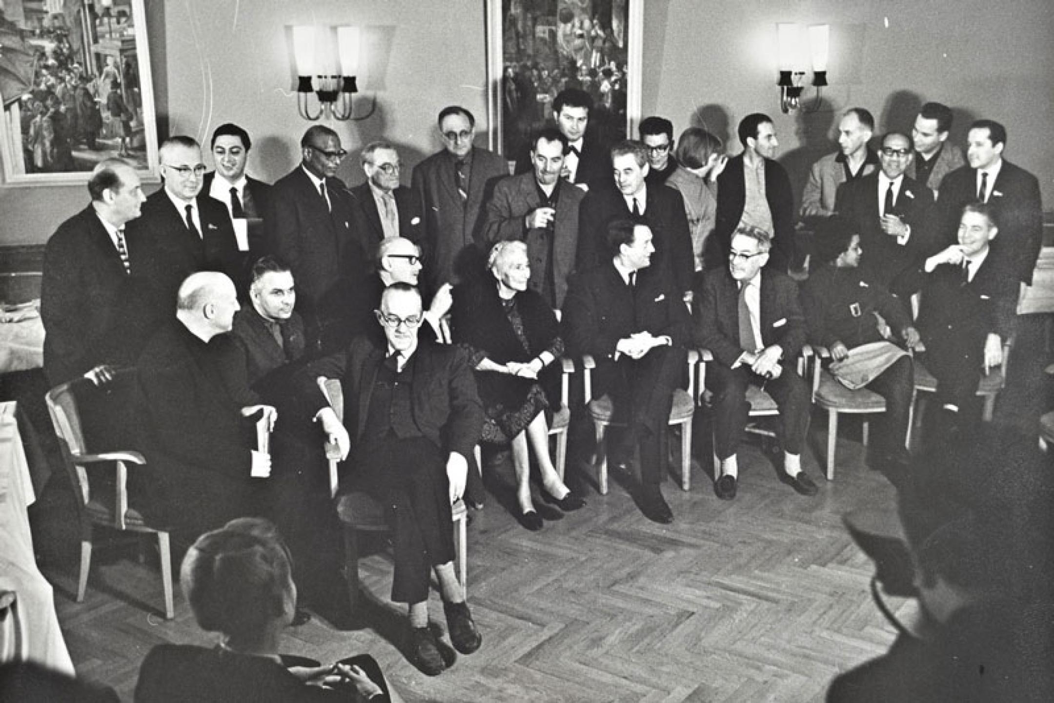 Rund zwei Dutzend Personen in zwei Reihen (vorne sitzend, dahinter stehend) bei einer Pressekonferenz.
