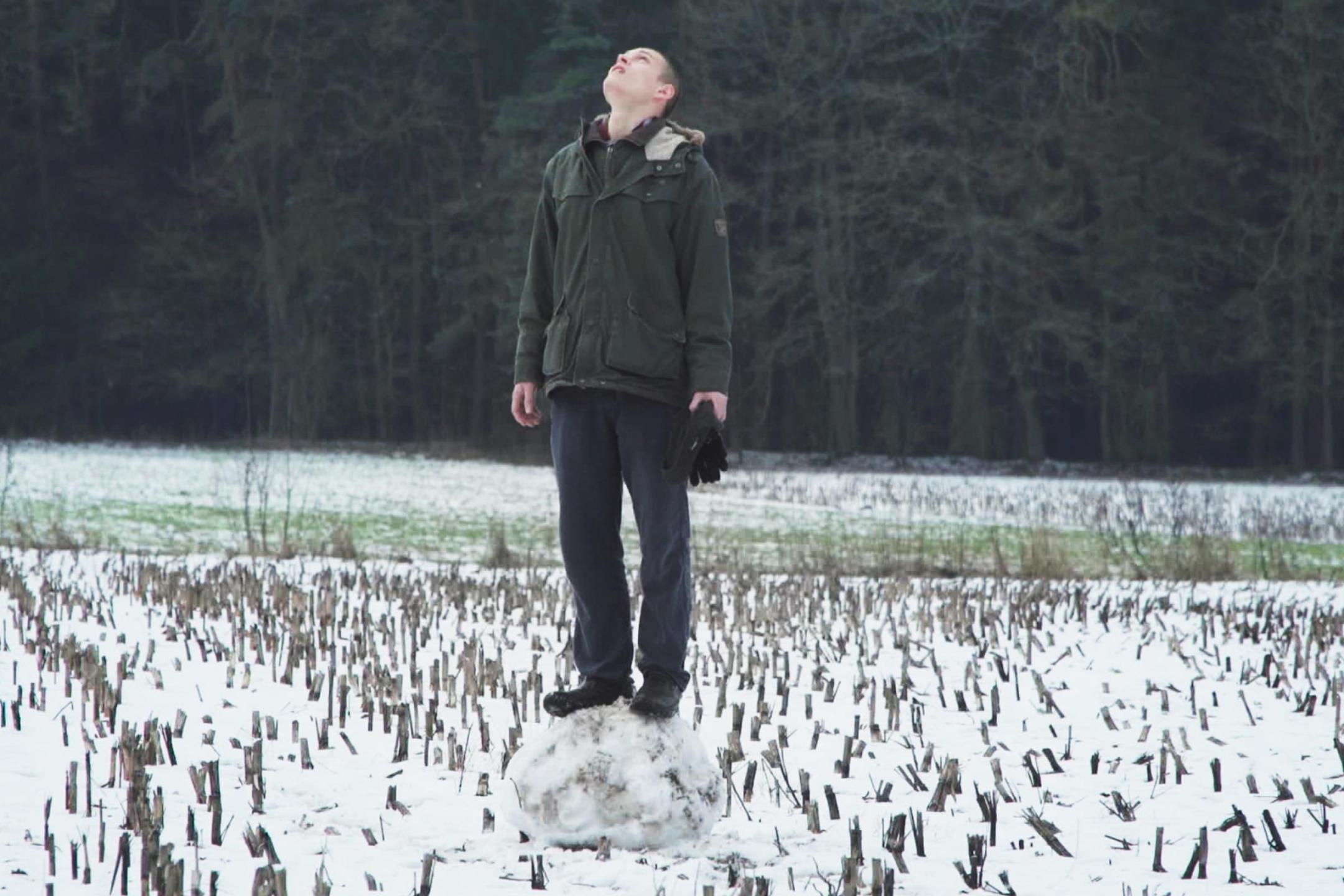 Ein junger Mann steht in einem mit Schnee bedeckten Stoppelfeld und blickt nach oben.