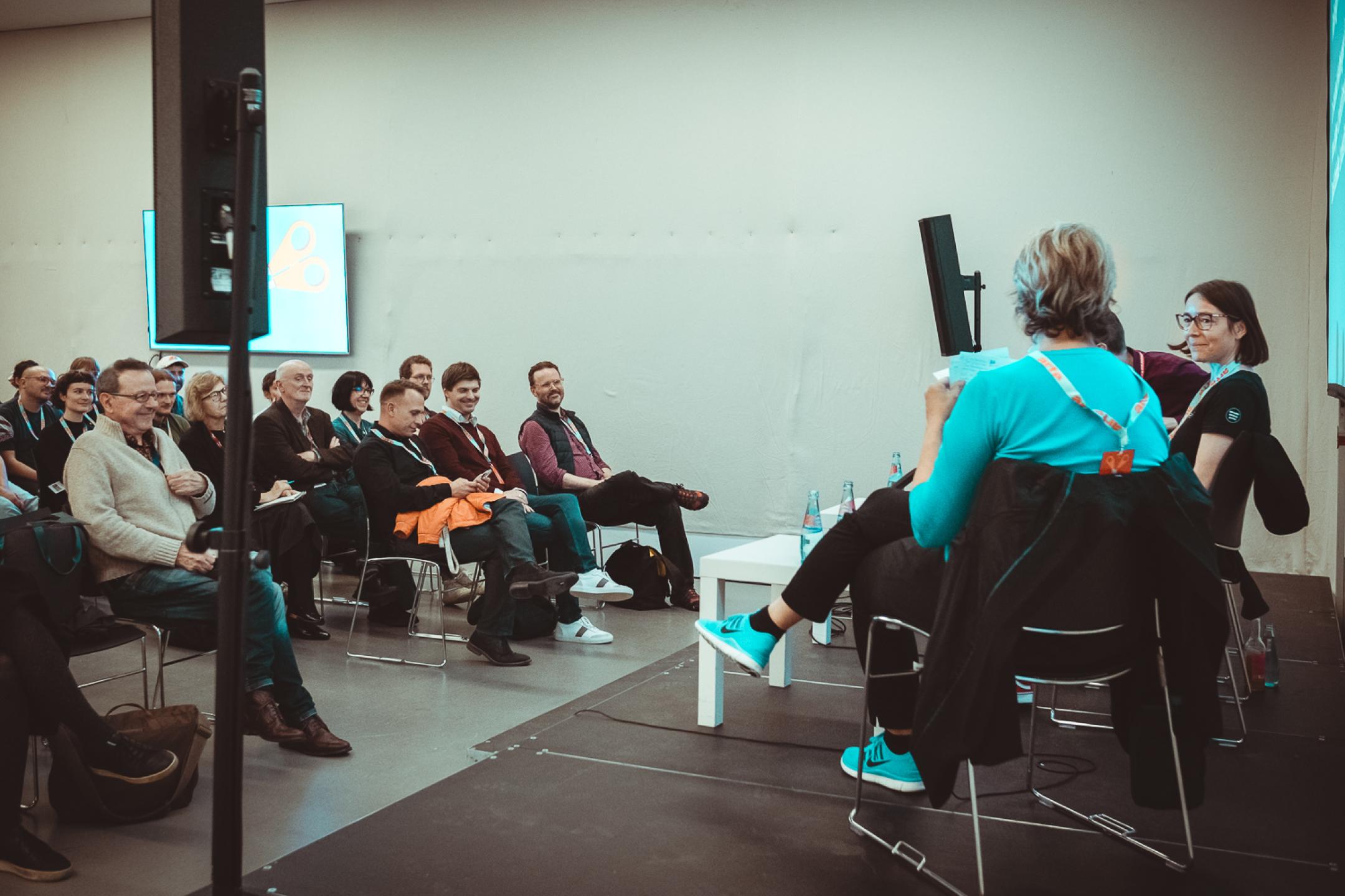 In front of an audience, several people are sitting on a stage