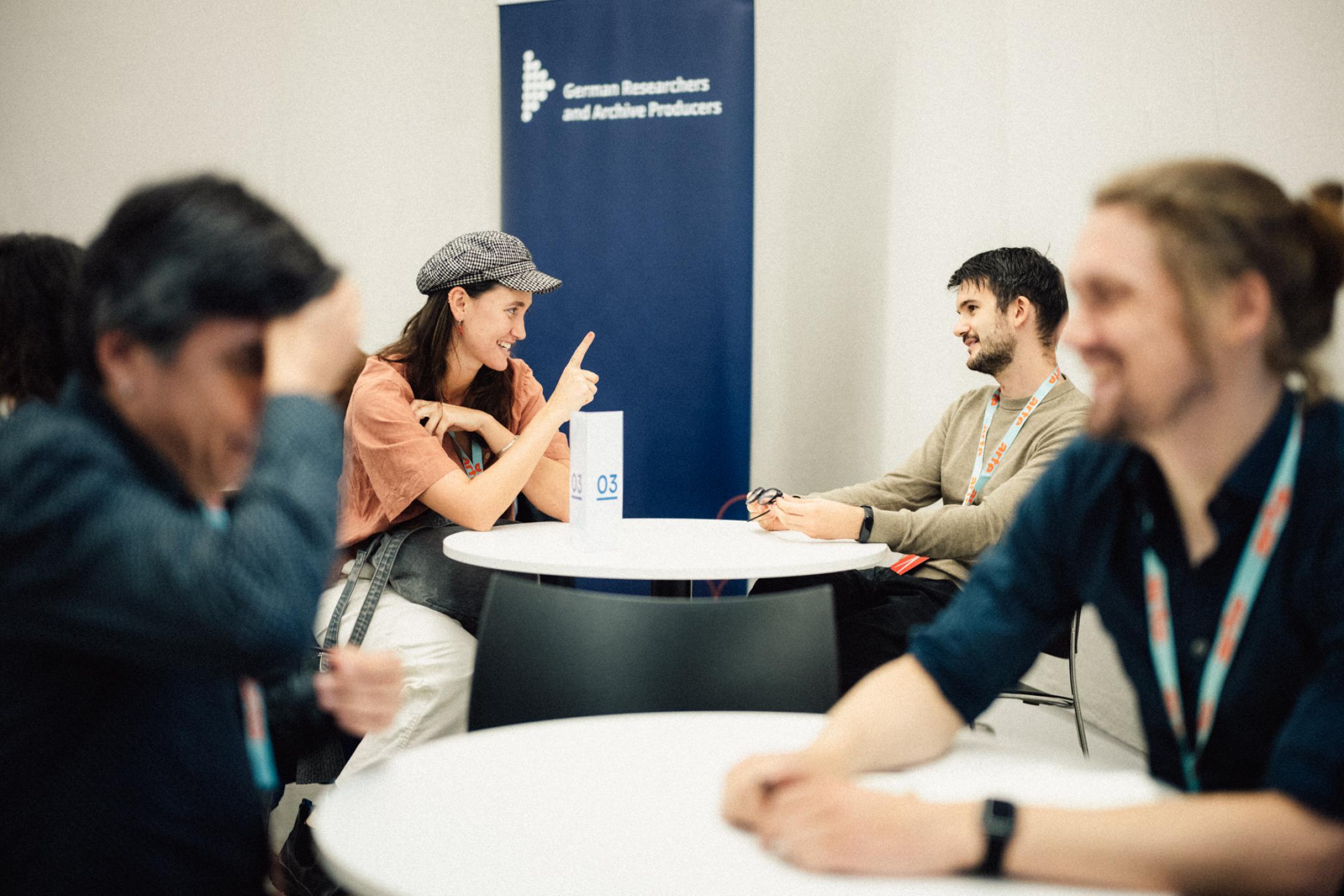 Two people sitting at a desk in conversation, a woman is playfully raising her finger 