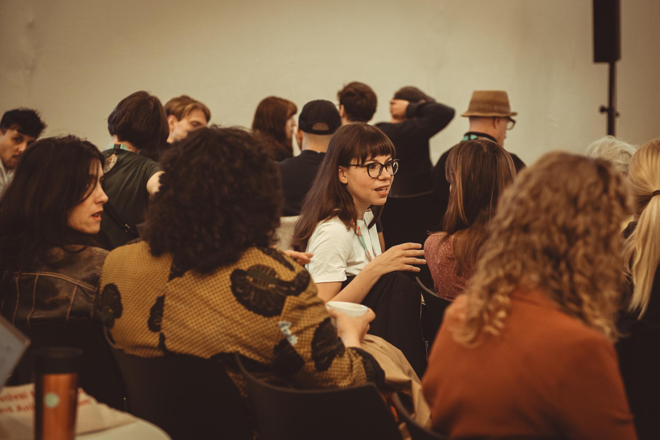 In an audience, a woman is turning to the person next to her and talks to her animatedly