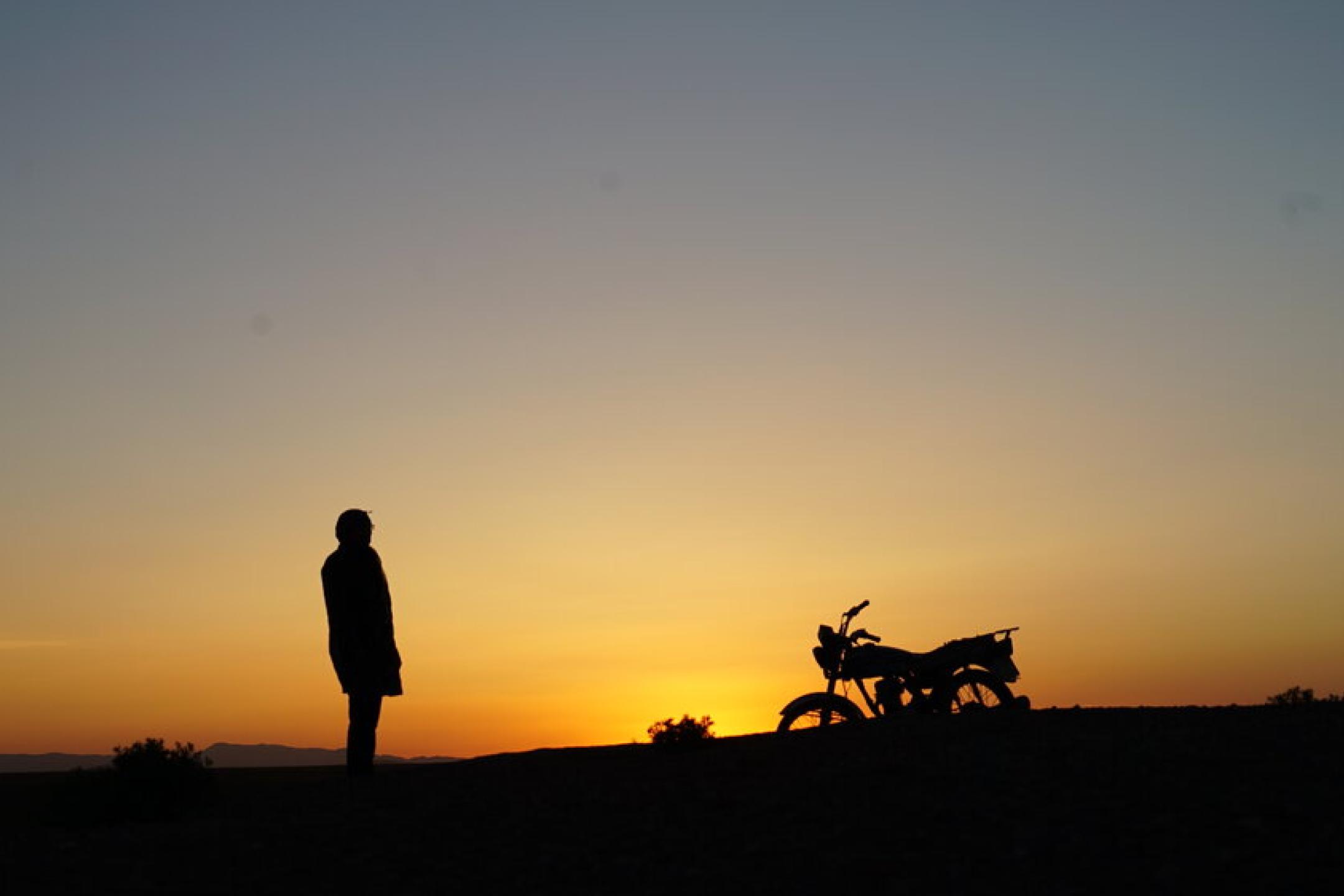 in front of a sunset, the silhouettes of a person and a motorbike are visible