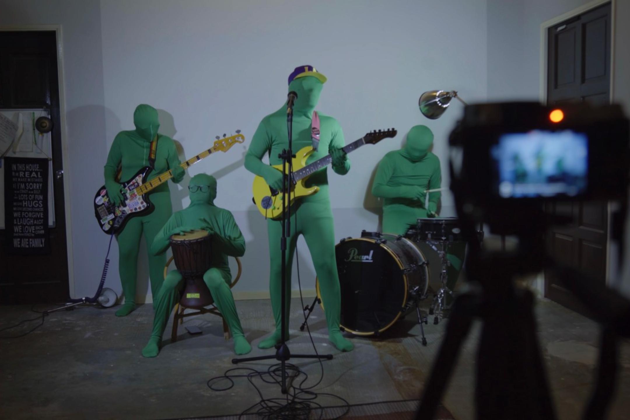 A rock band playing their instruments but everyone is wearing a green screen suit