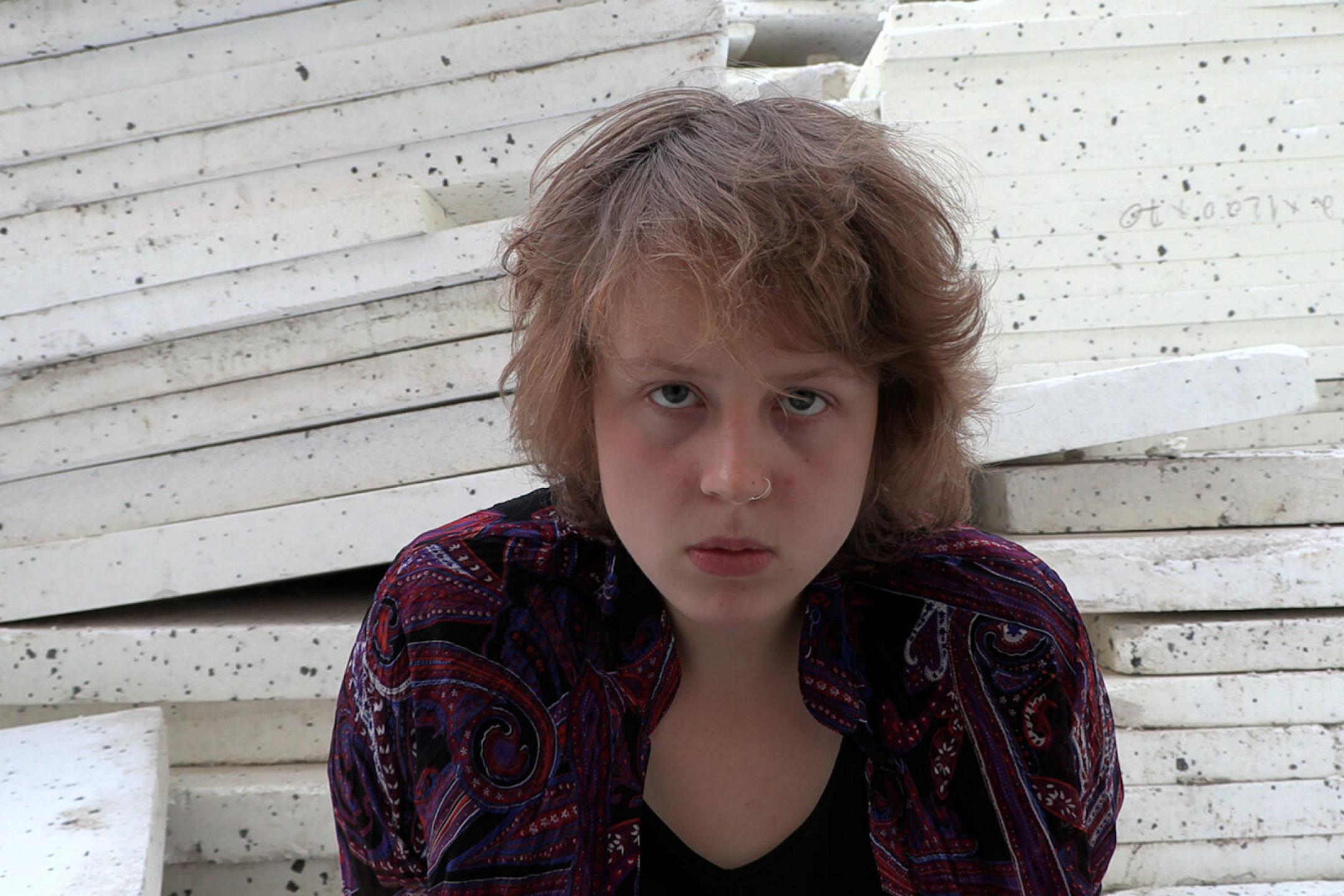 A young woman is leaning towards the camera and looks very earnestly directly at the view