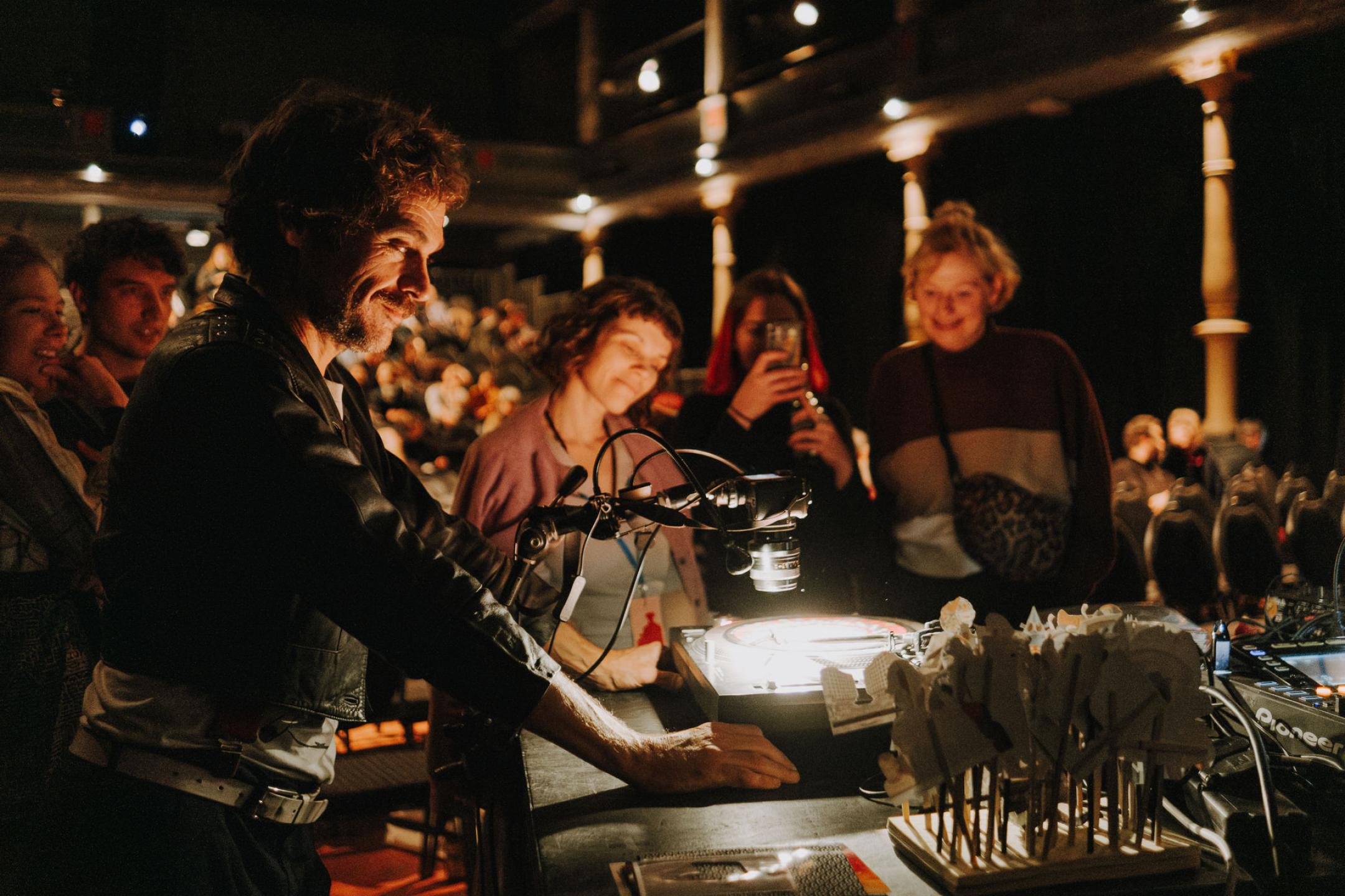 Mehrere Menschen stehen im Kinosaal um einen Tisch, auf dem eine Kamera auf einen angeleuchteten Schallplattenspieler gerichtet ist