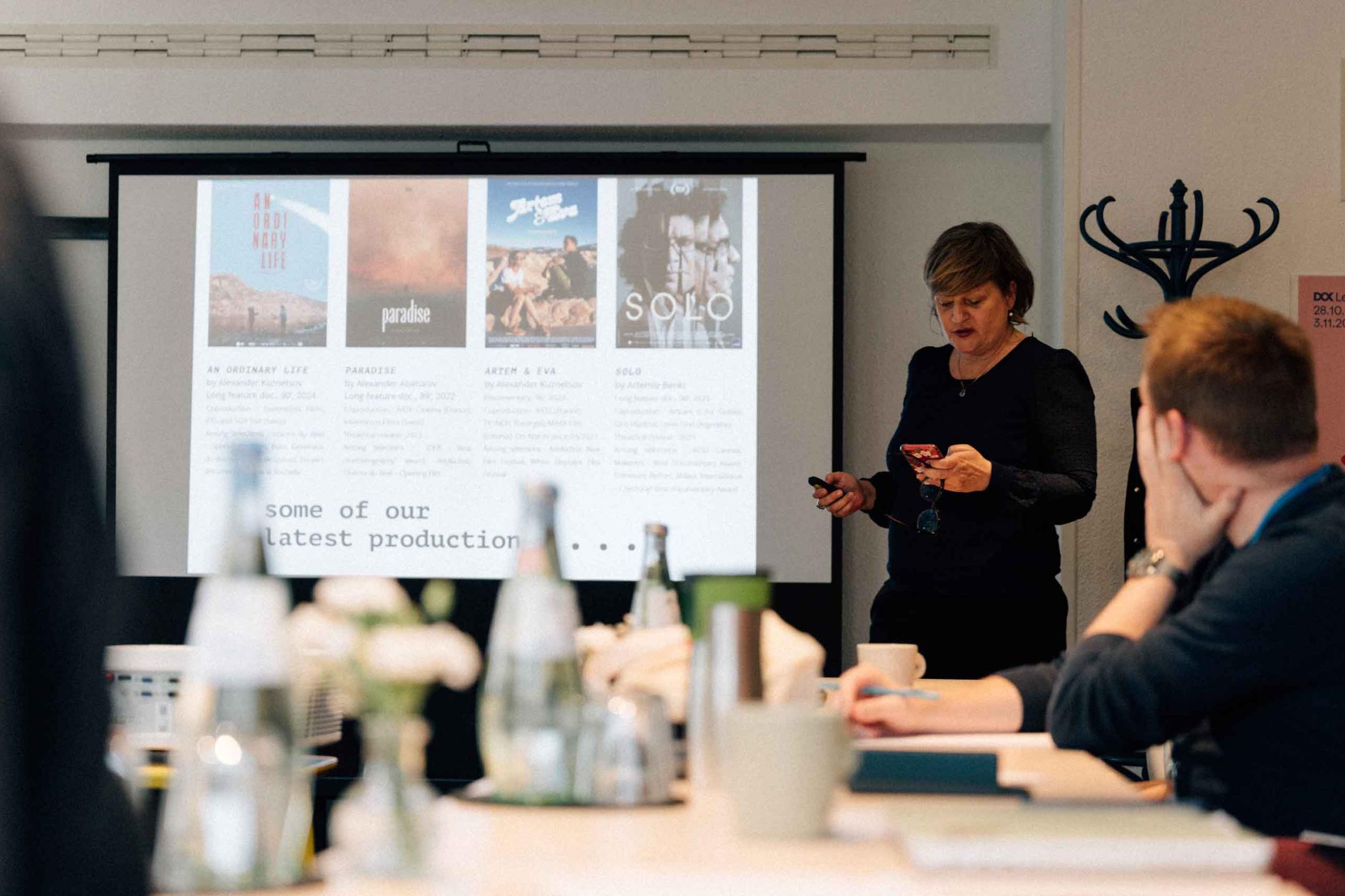 A participant of the Animation lab stands in front of the workshop group's table to present her latest film productions on a screen