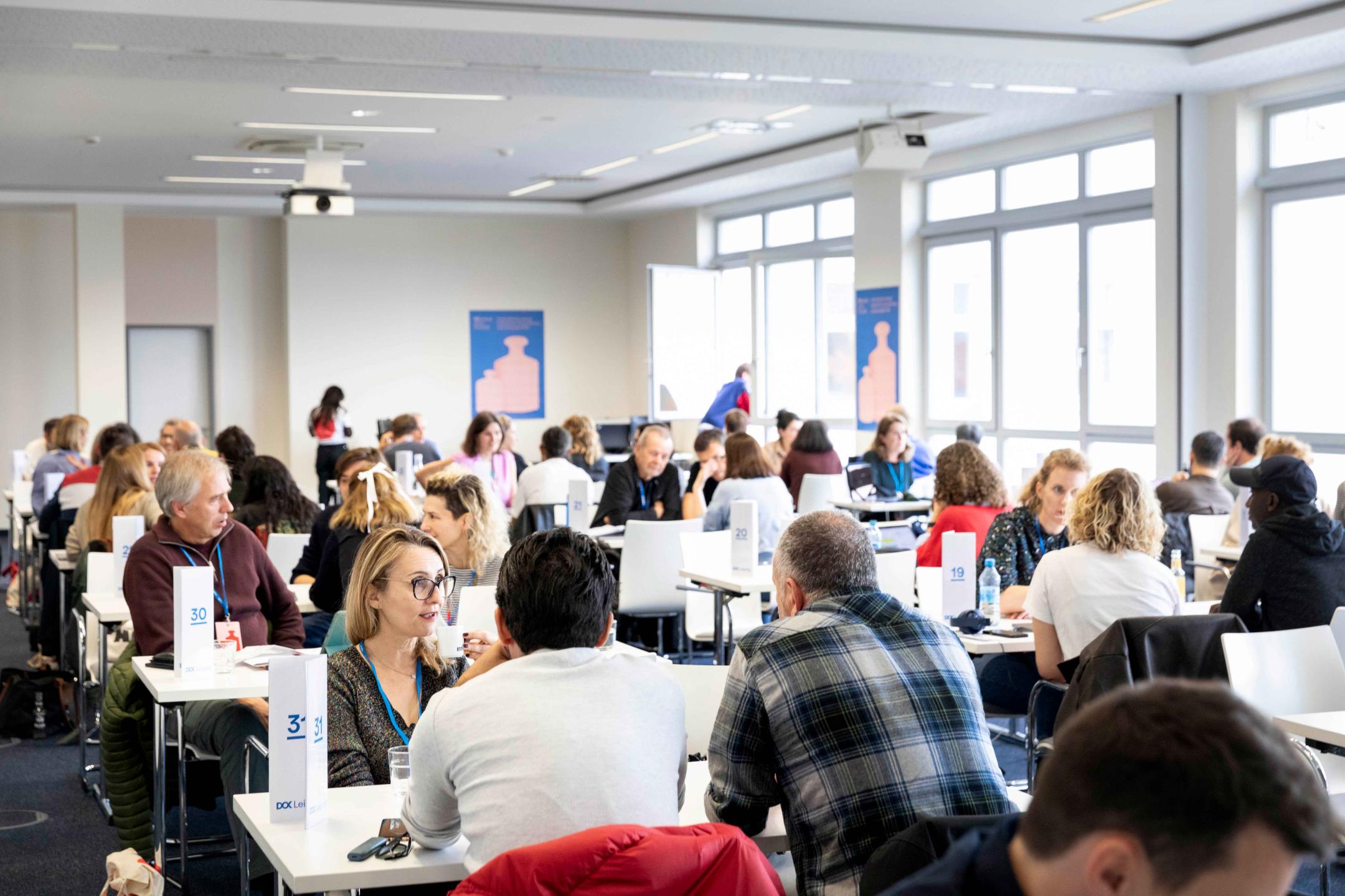 A room full of people sitting at tables in small groups talking to each other