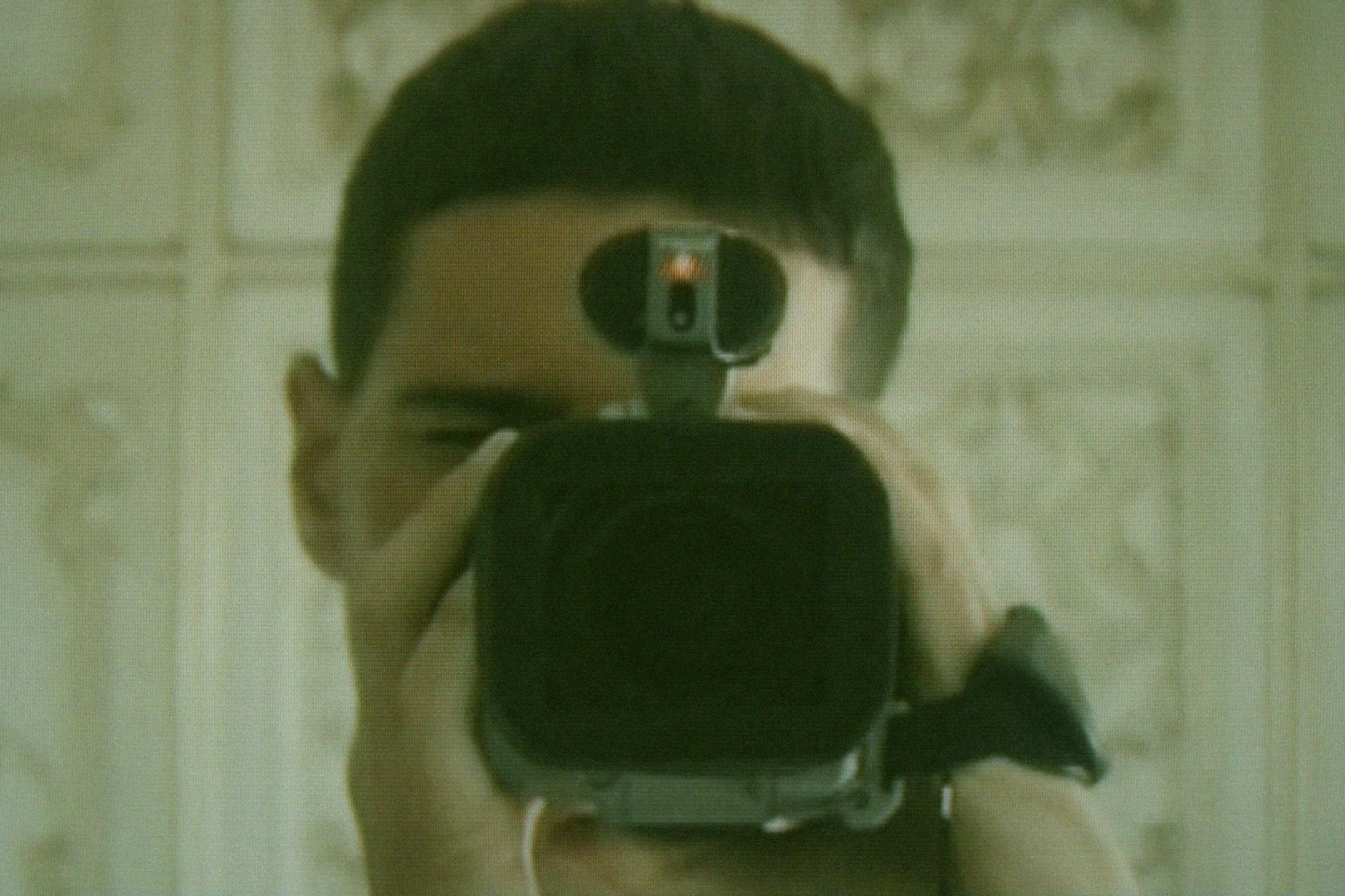 Film still "A Near Thing", close up of person holding a camera at viewer