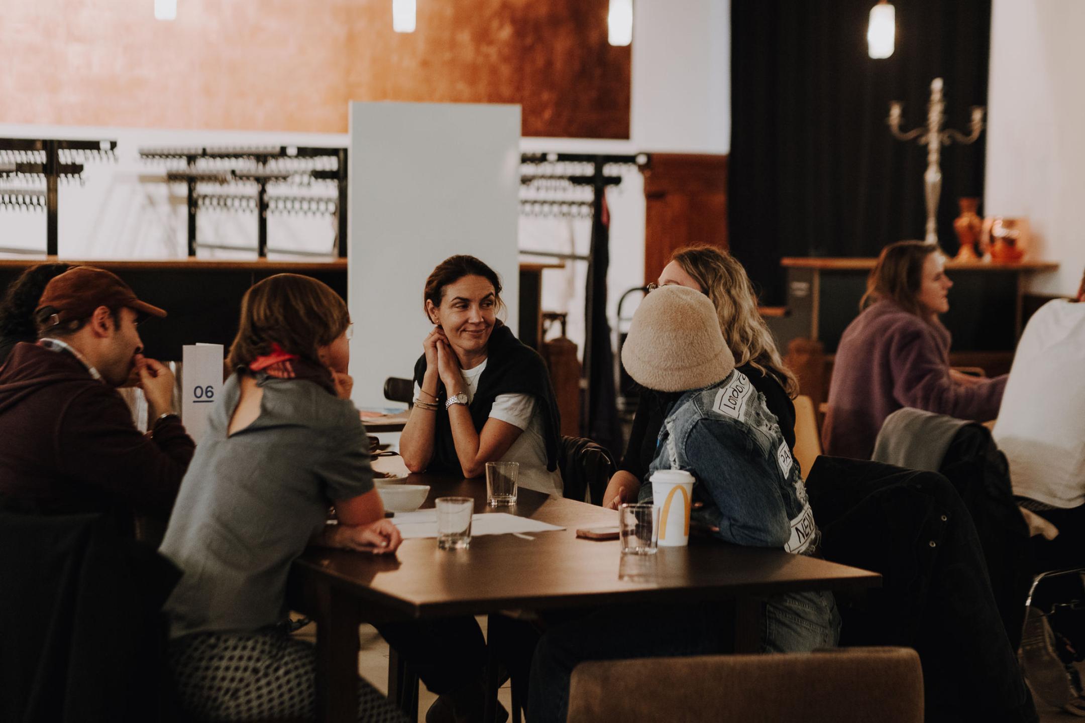 Vier Personen sitzen an einem Tisch, eine Person mit Gesicht zur Kamera lächelnd