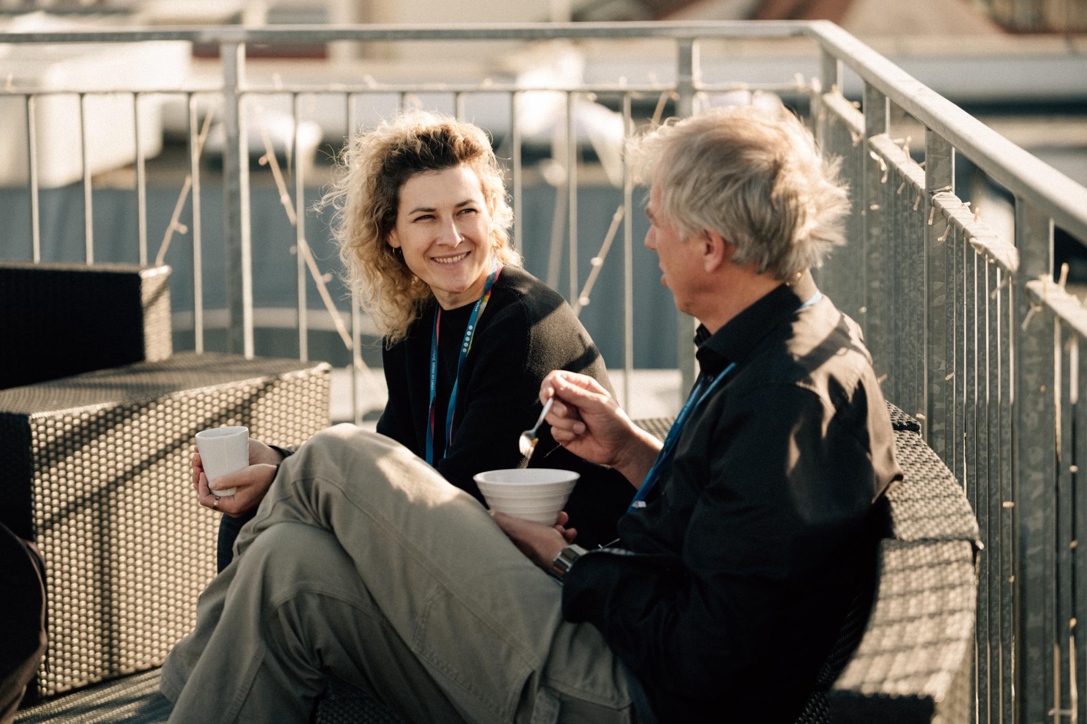 Frau und Mann sitzen auf einem Balkon, unterhalten sich und trinken Kaffee