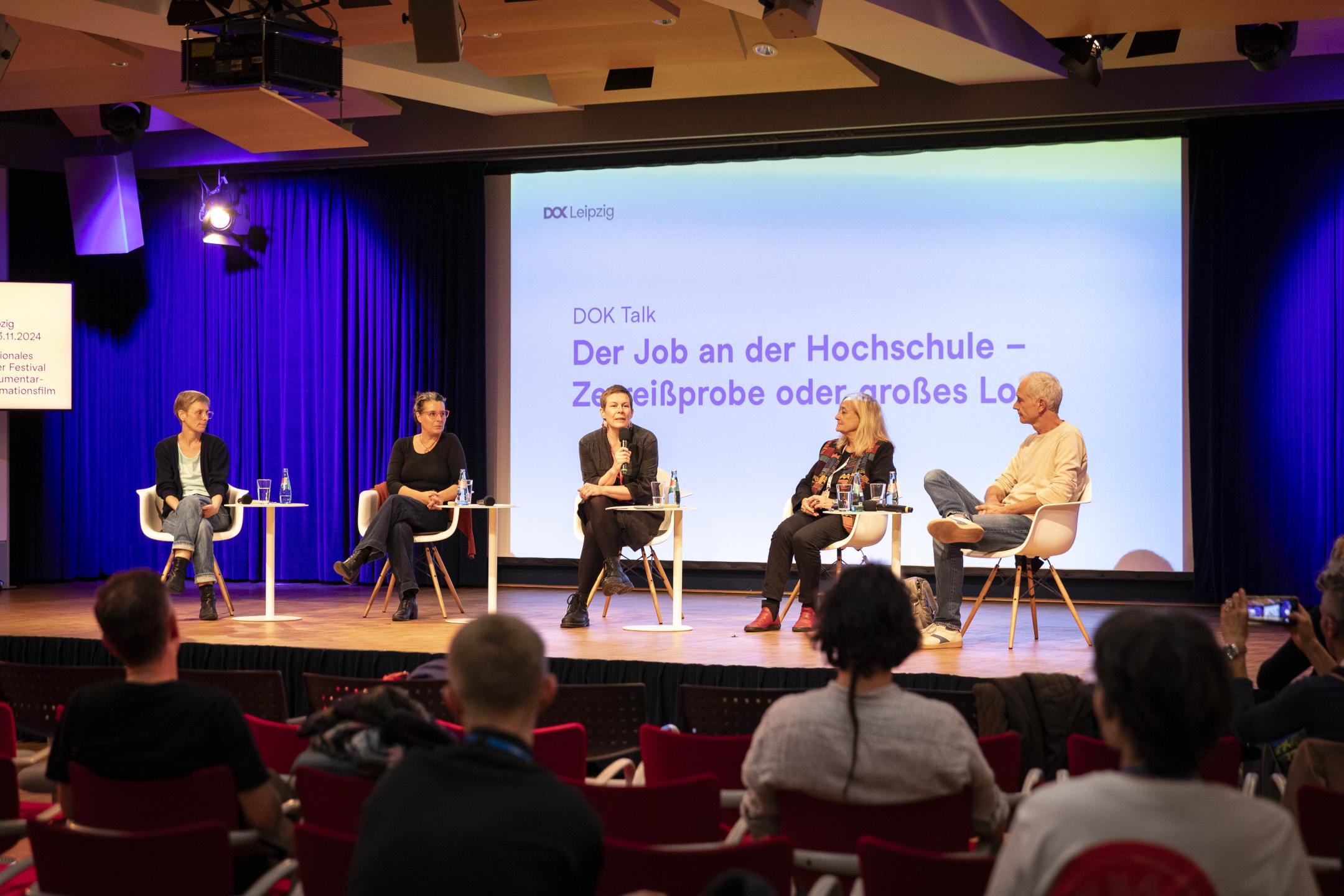 Personen sitzen auf einer Bühne, Publikum vor ihnen